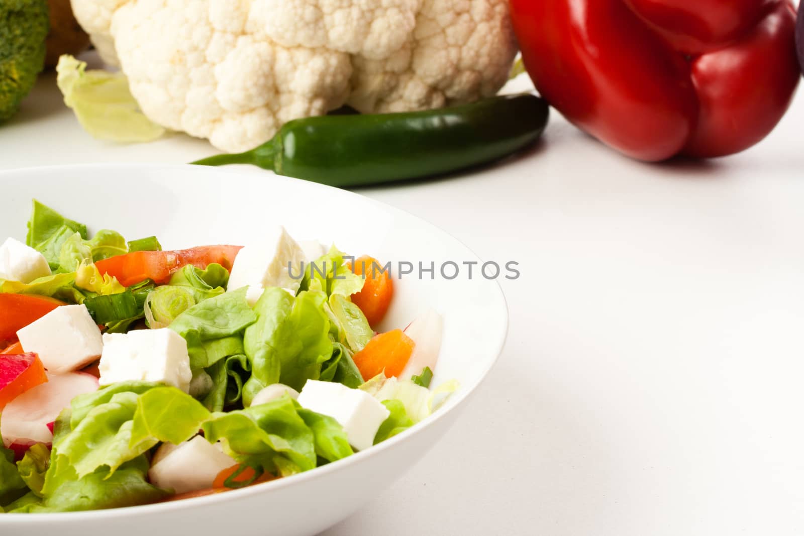 vegetable salad in white bowl with different vegetables in the background