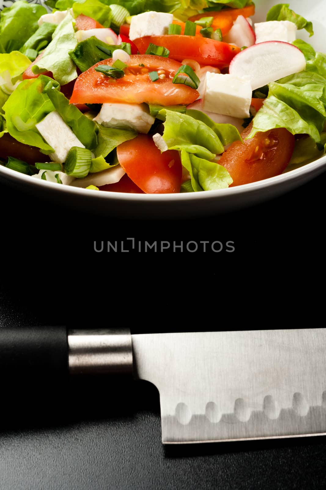 vegetable salad in a white bowl with big knife on black background