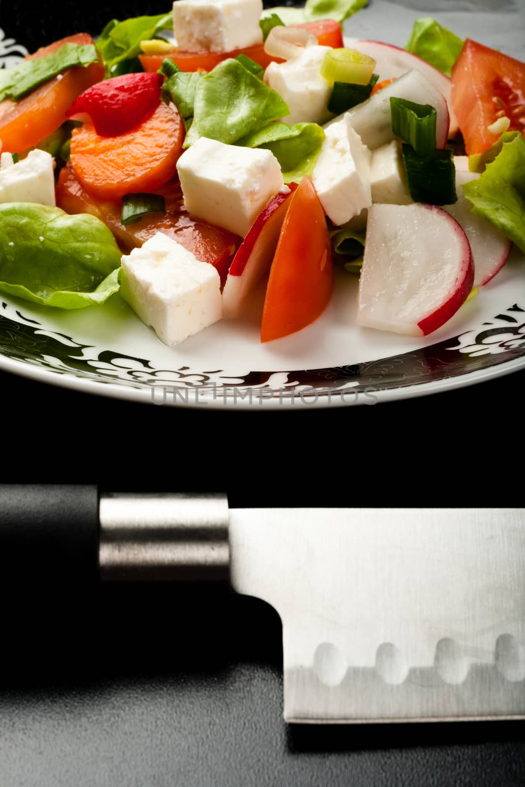 vegetable salad in a white bowl with big knife on black background