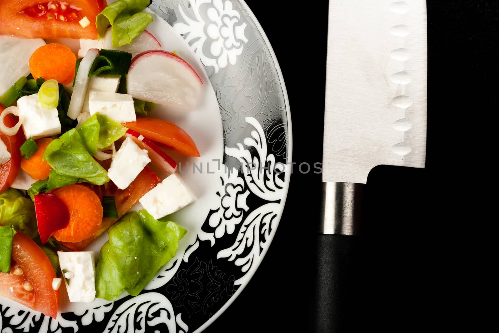 vegetable salad in a white bowl with big knife on black background