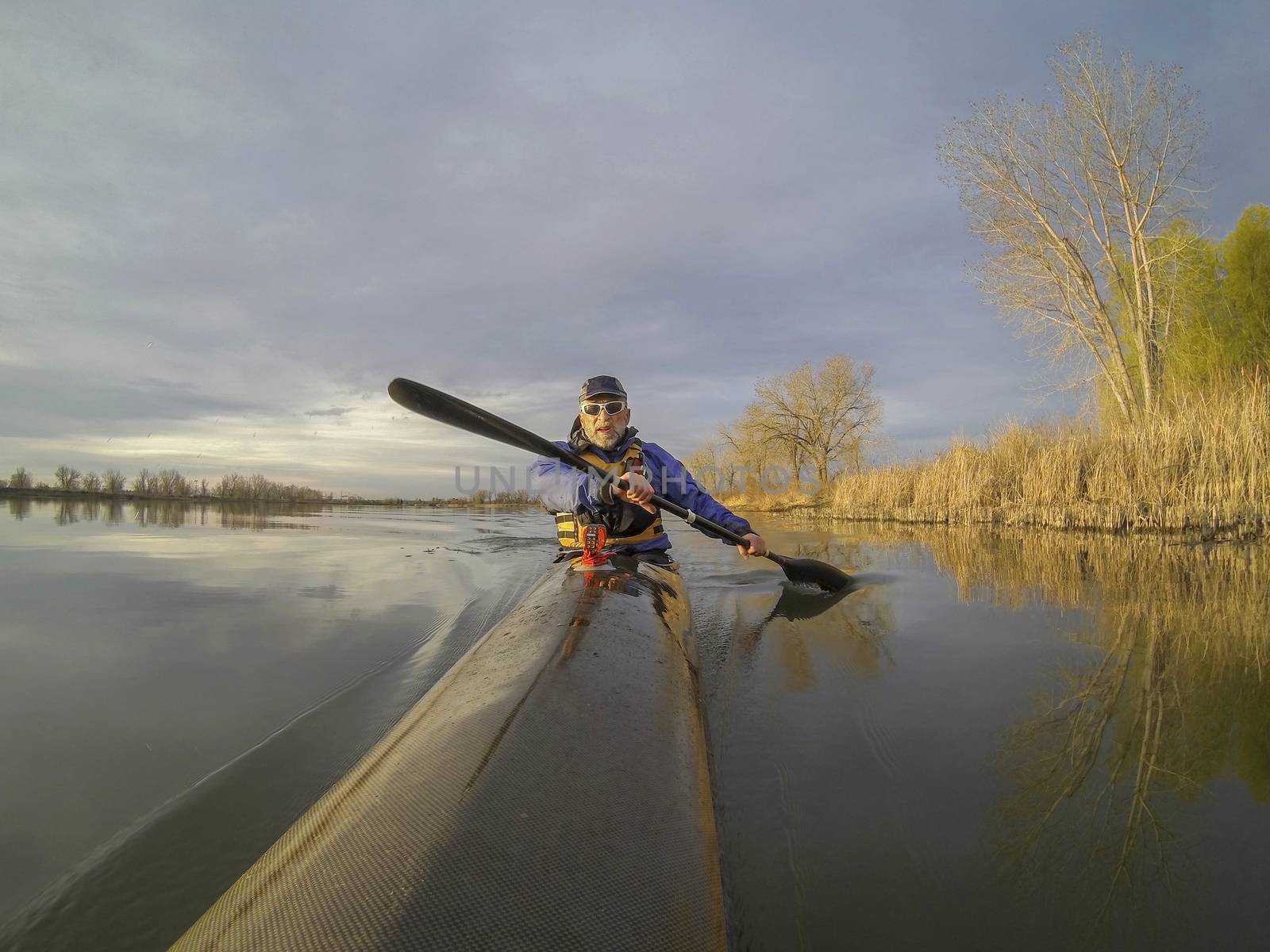 senior male paddler enjoys morning workout in a slim racing kayak on a calm lake in Colorado