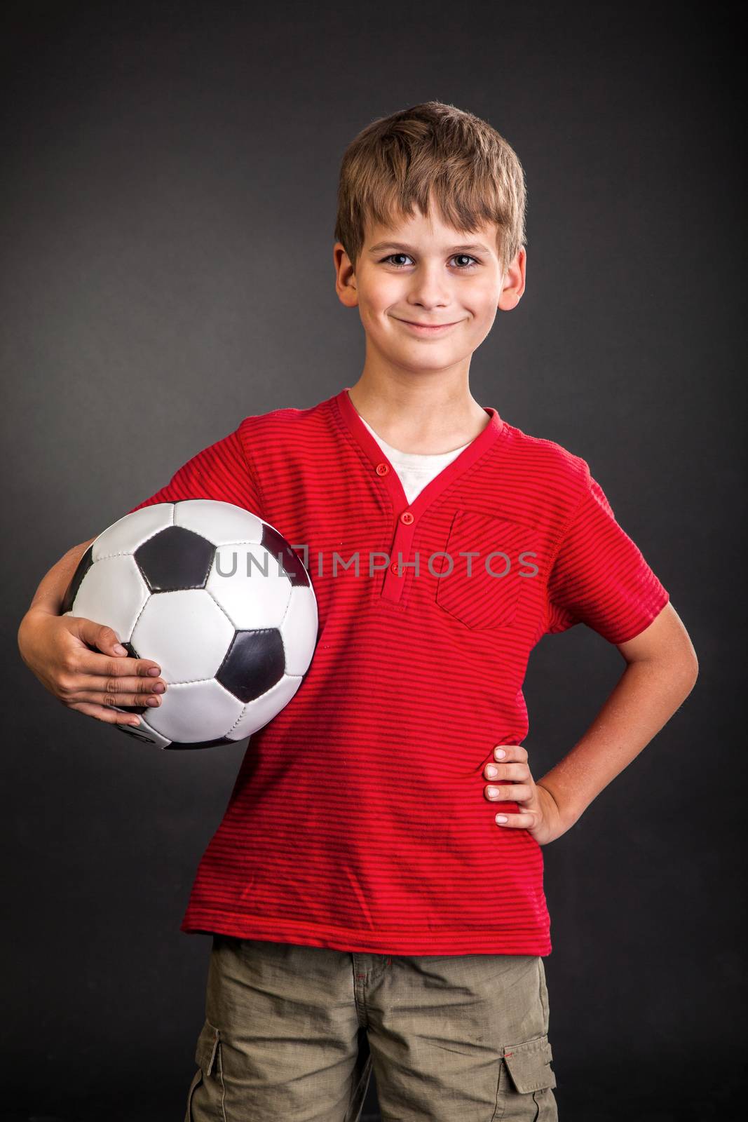 Cute boy is holding a football ball made of genuine leather isolated on a black background. Soccer ball