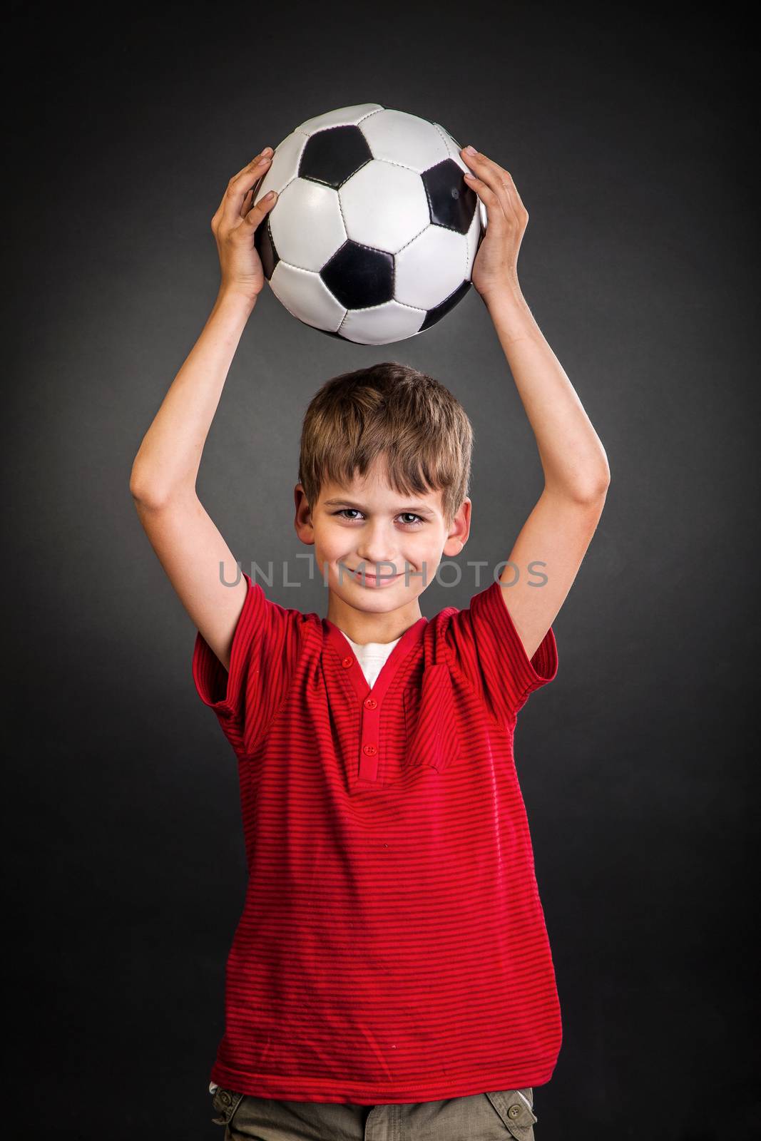 Cute boy is holding a football ball made of genuine leather isolated on a black background. Soccer ball