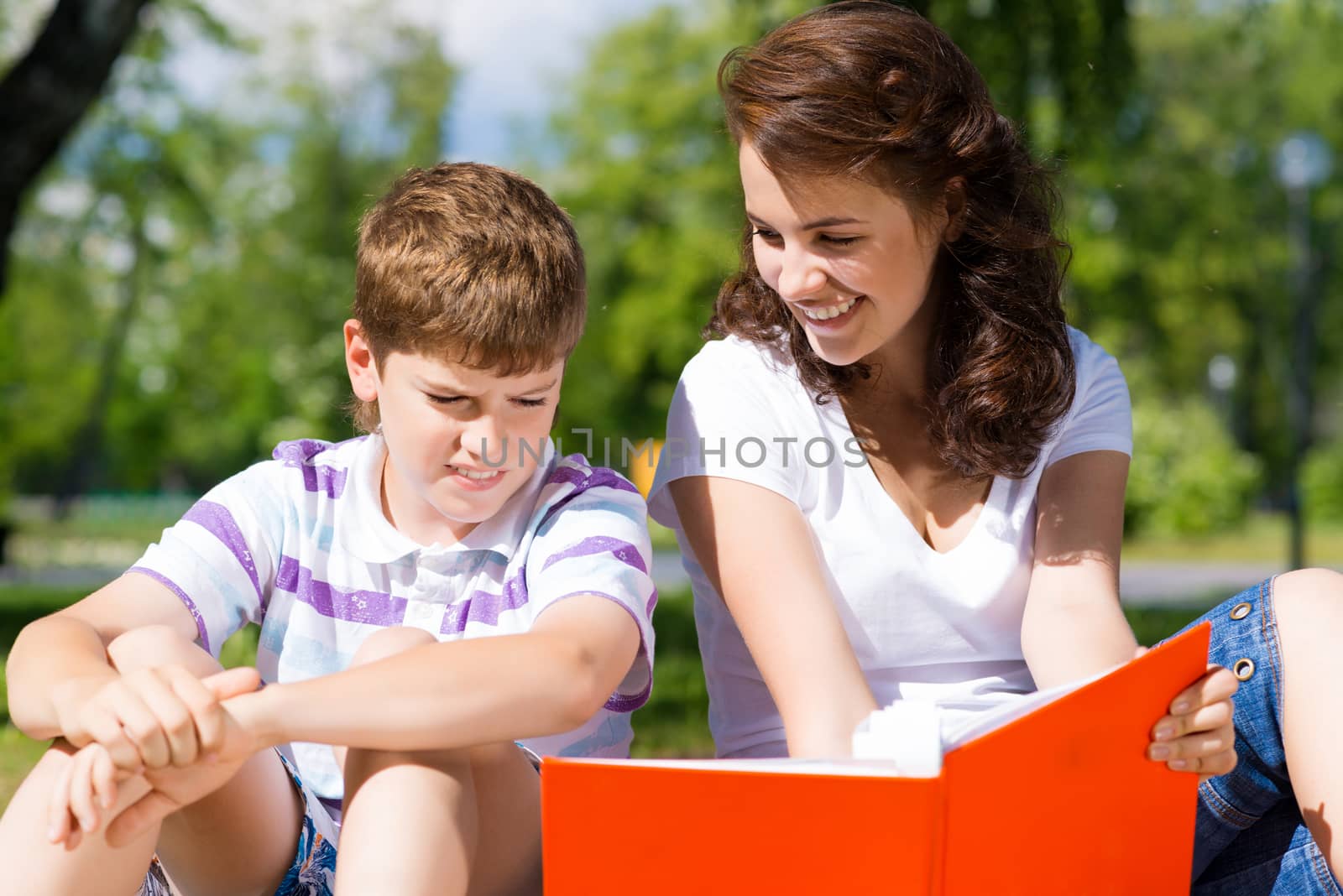 boy and a woman in a summer park reading a book together