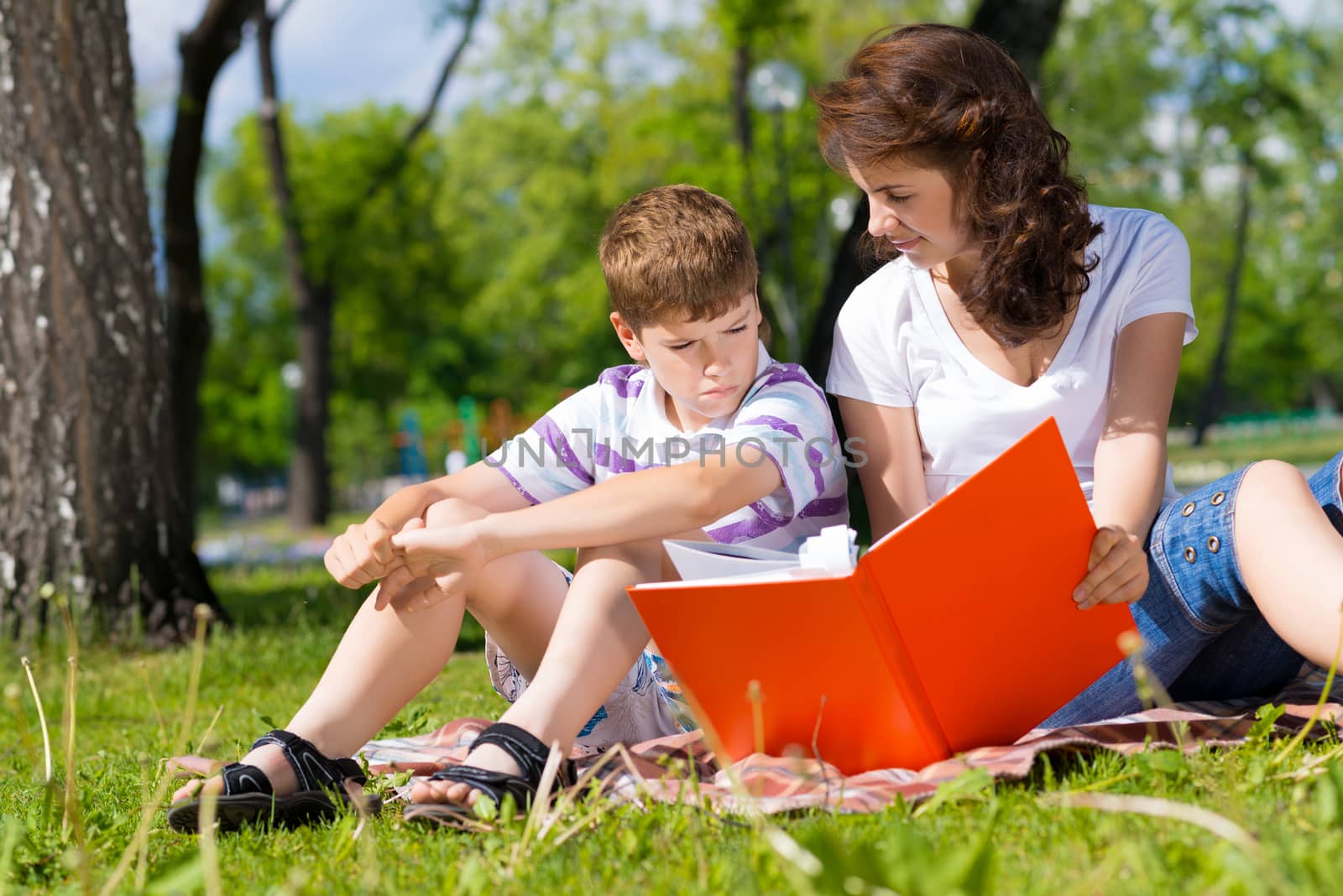 boy and a woman in a summer park reading a book together