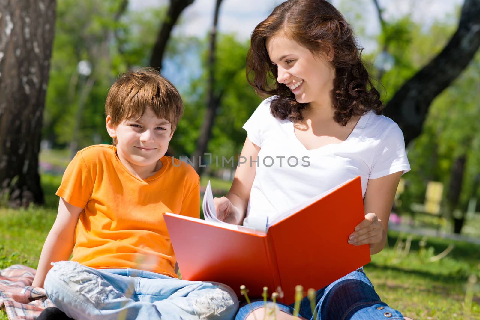 boy and a woman in a summer park reading a book together