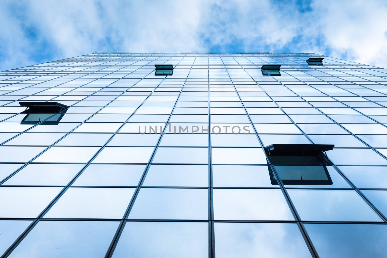 Modern facade of glass and steel with open window reflecting sky and clouds.