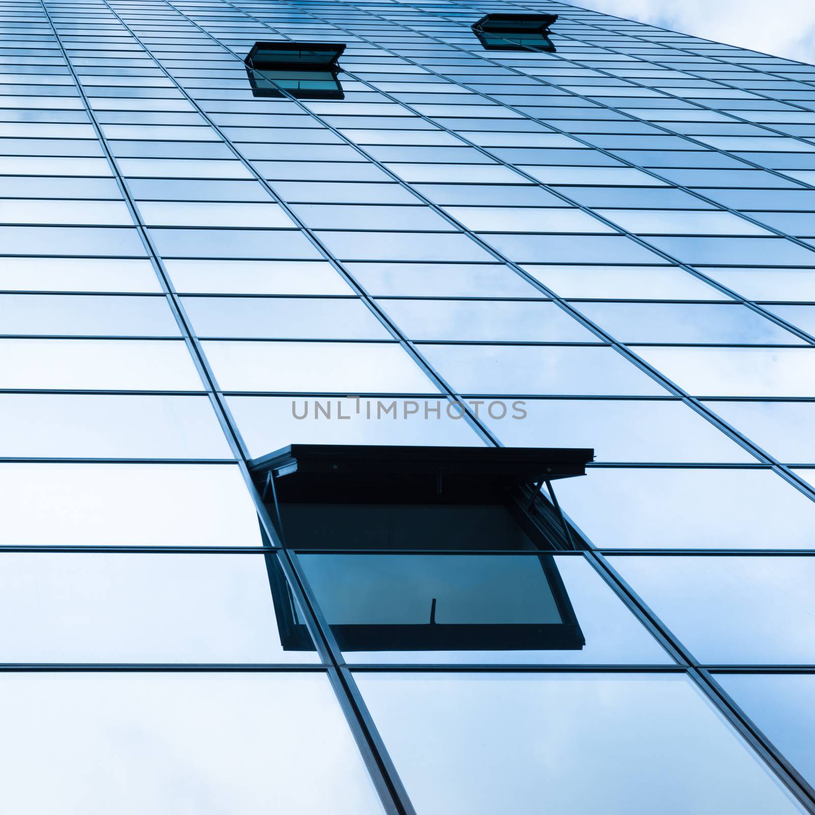 Modern facade of glass and steel with open window reflecting sky and clouds.