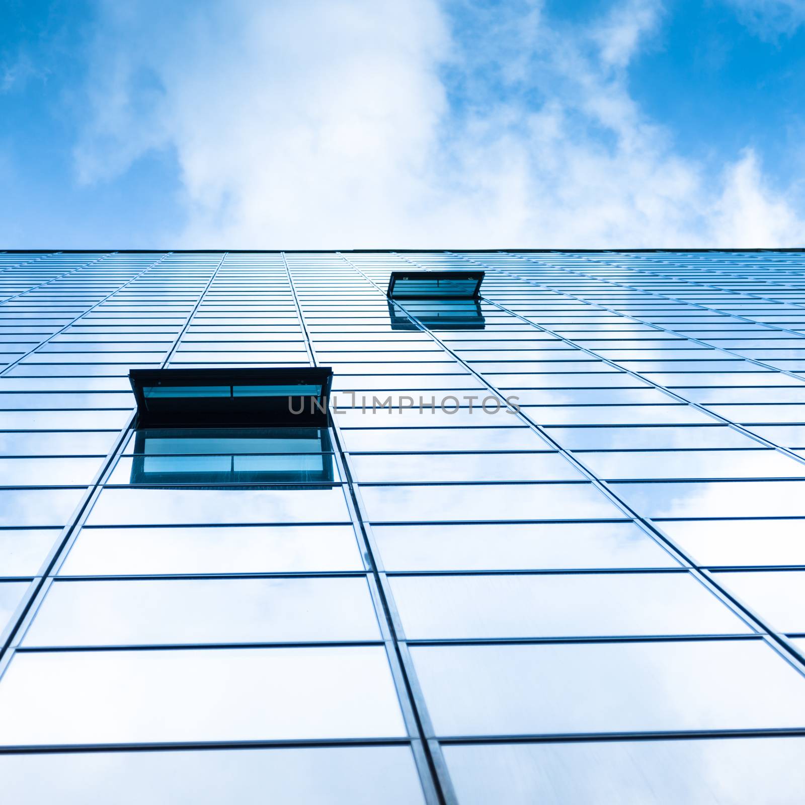 Modern facade of glass and steel with open window reflecting sky and clouds.