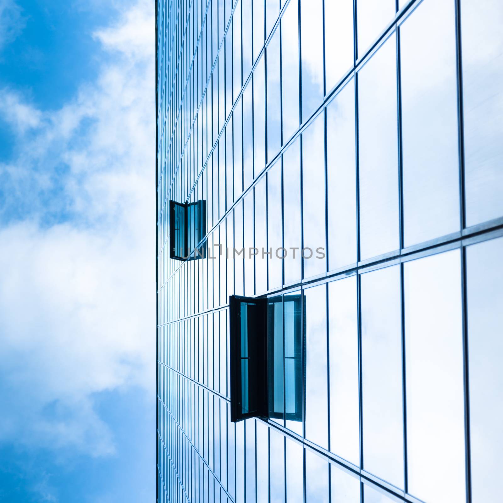 Modern facade of glass and steel with open window reflecting sky and clouds.