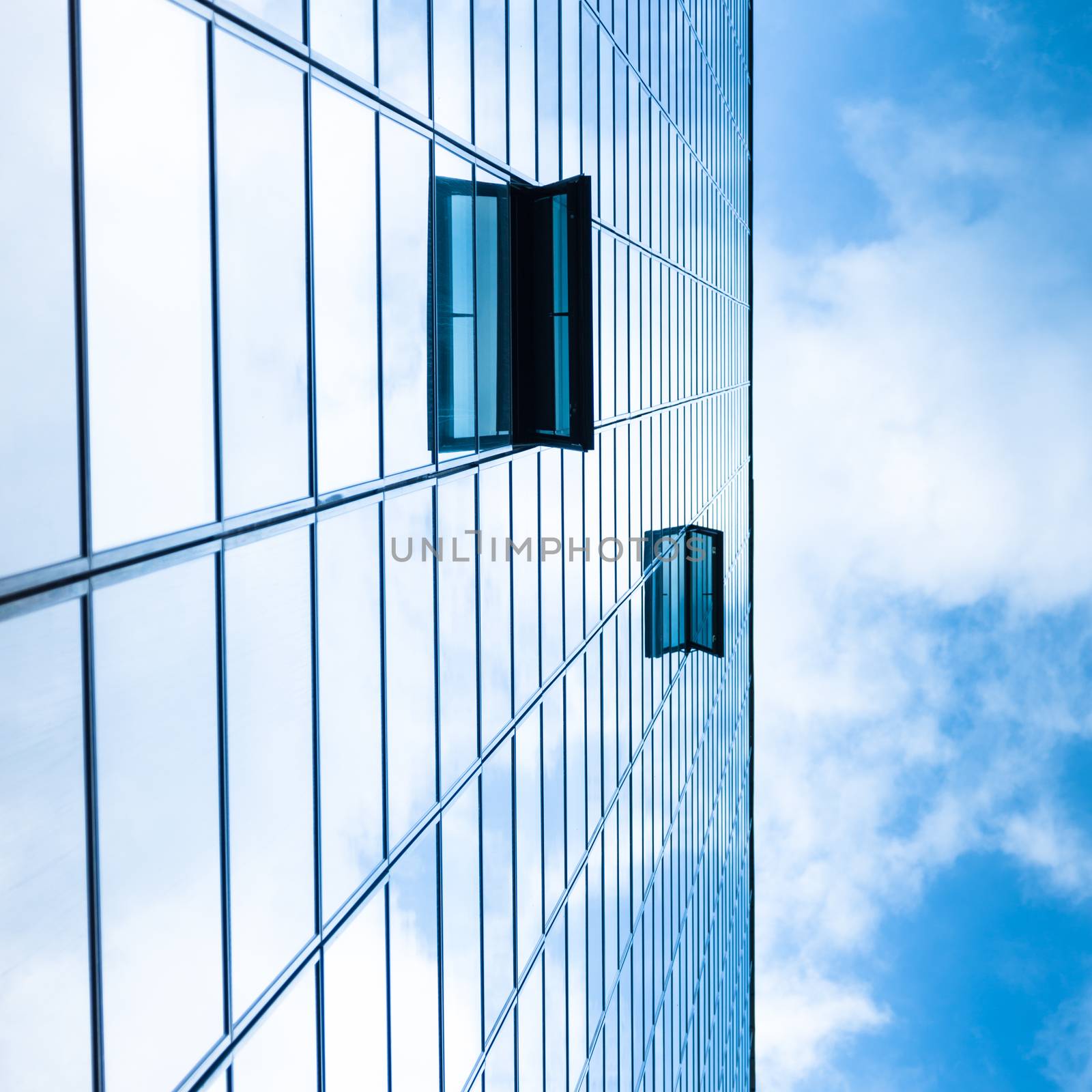 Modern facade of glass and steel with open window reflecting sky and clouds.