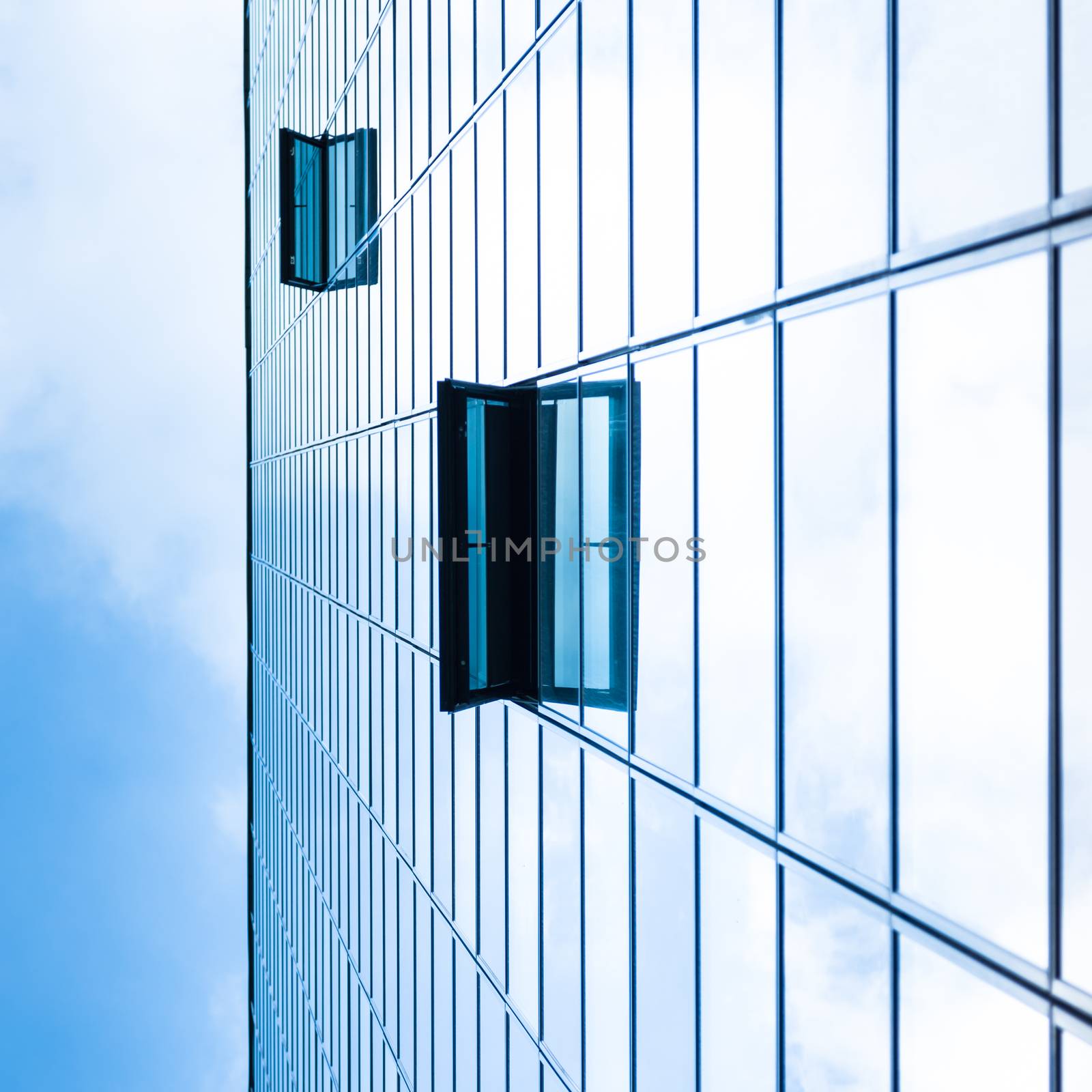 Modern facade of glass and steel with open window reflecting sky and clouds.