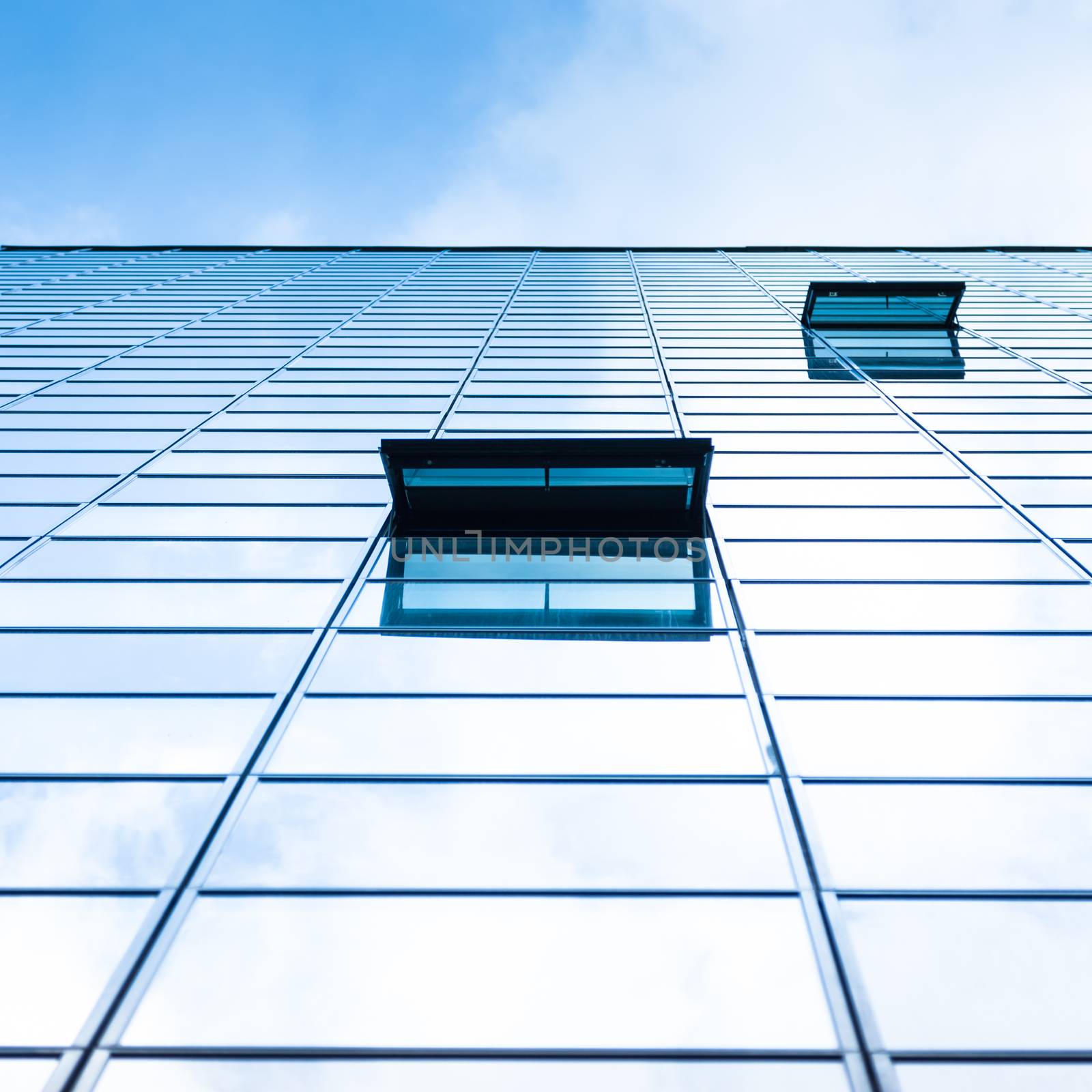 Modern facade of glass and steel with open window reflecting sky and clouds.