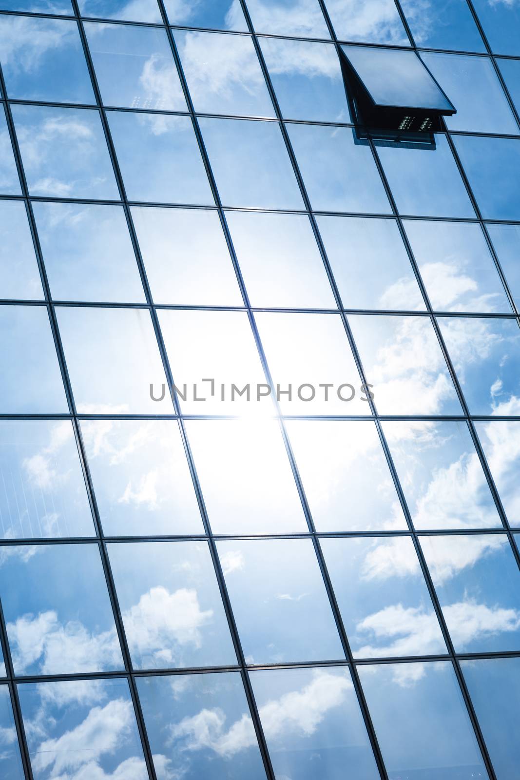 Modern facade of glass and steel with open window reflecting sky and clouds.