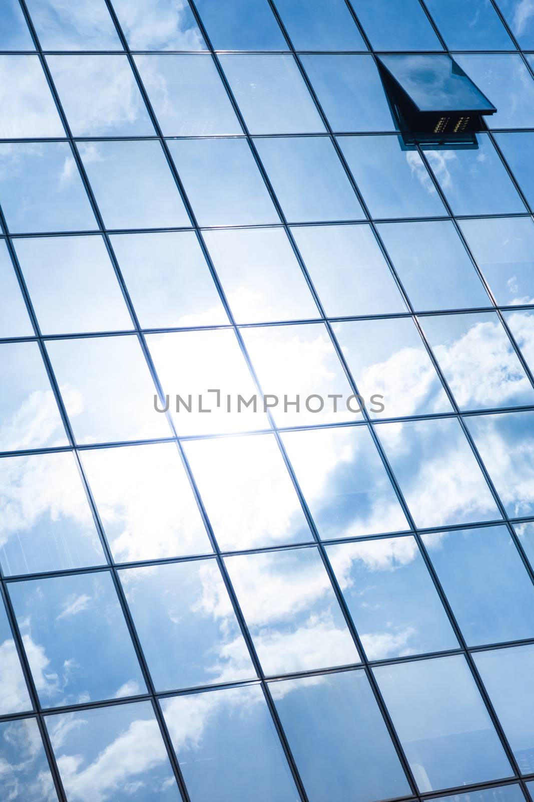 Modern facade of glass and steel with open window reflecting sky and clouds.