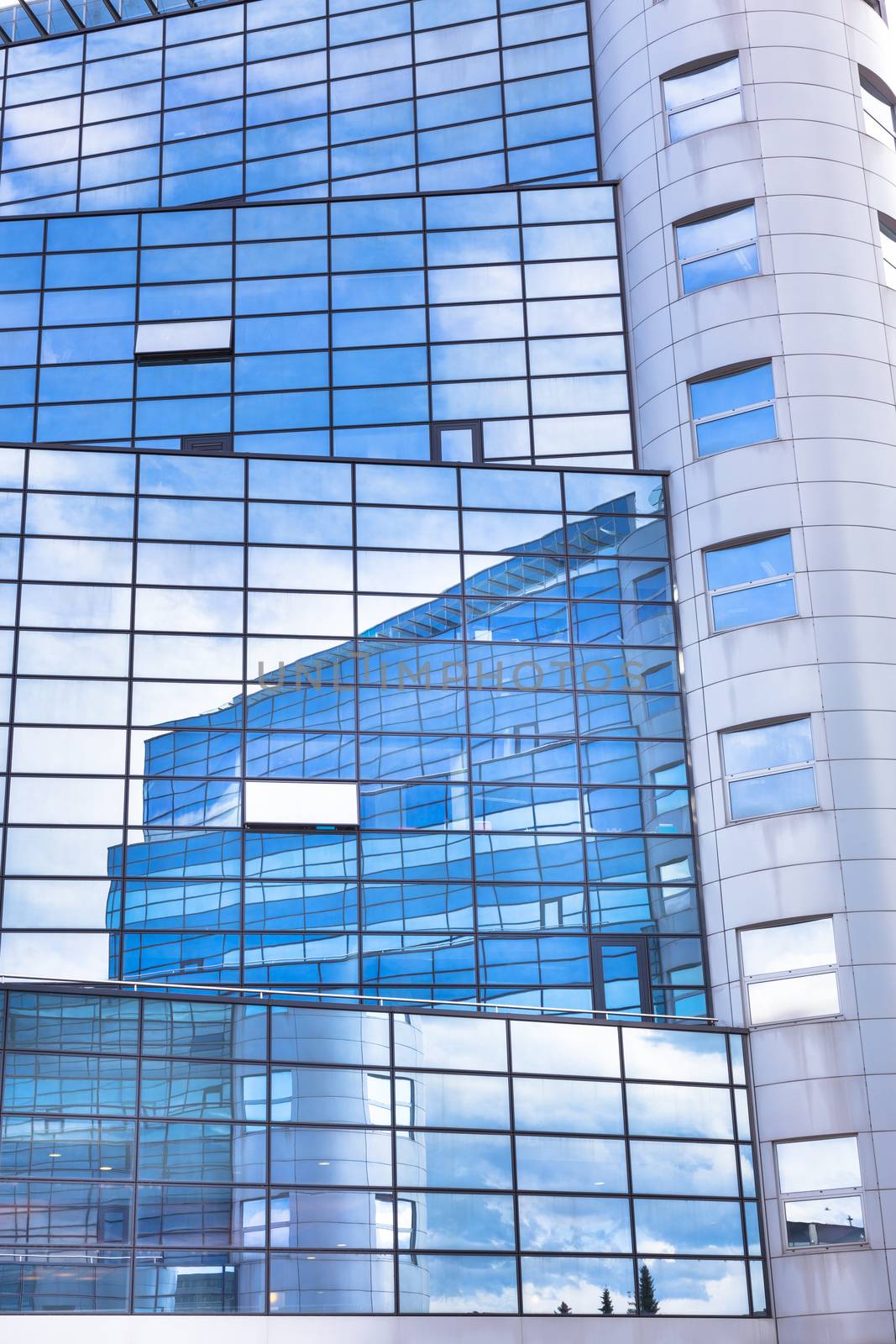 Modern facade of glass and steel with open window reflecting sky and clouds.