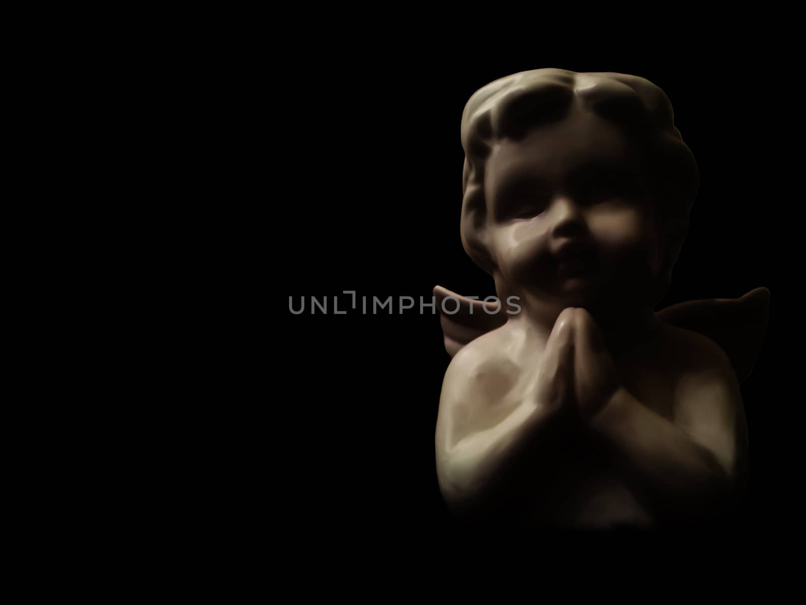 Statue of a small angel praying in the dark with available copyspace on the left.