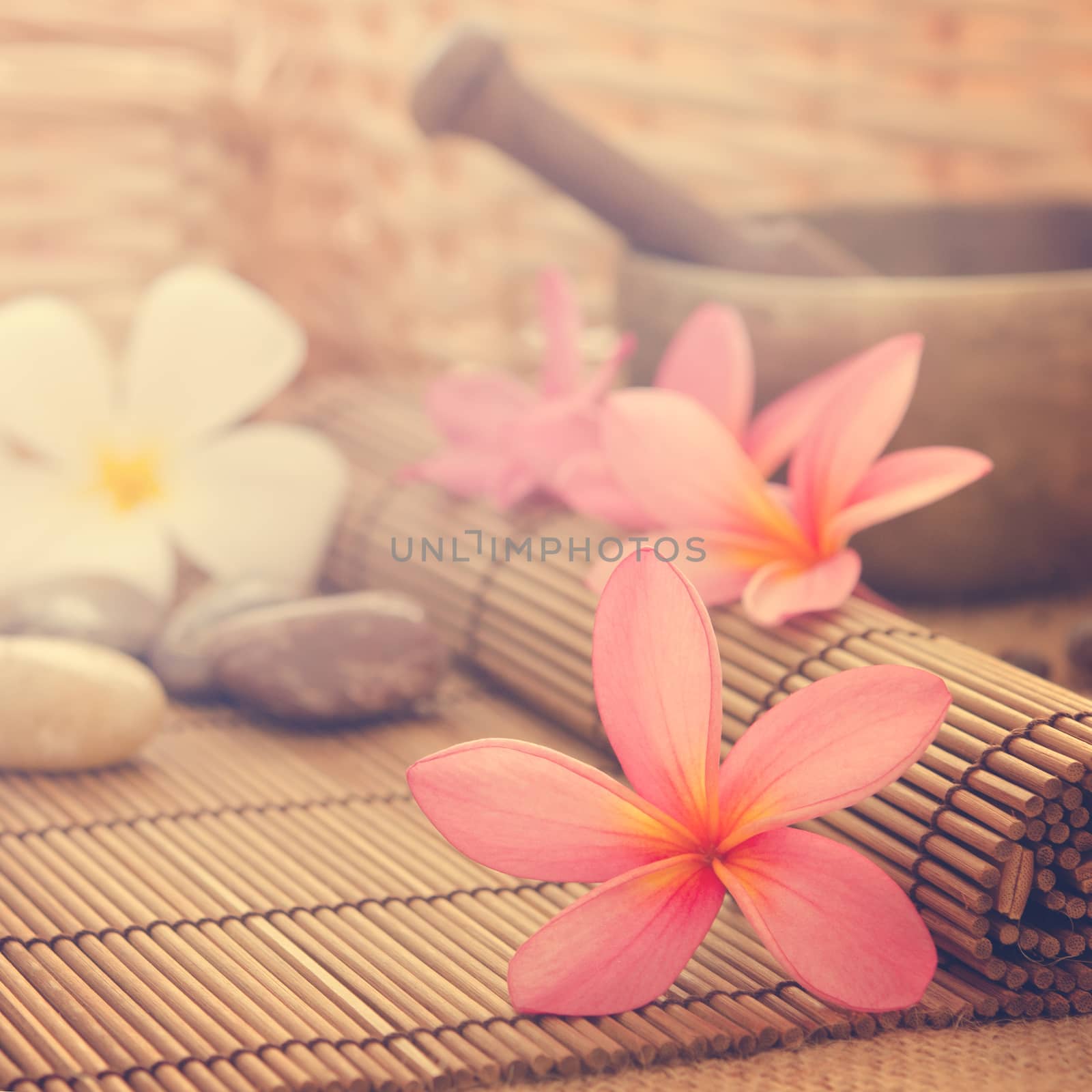 Spa setting, low light with ambient in vintage revival tone. Frangipani, hot and cold stone on bamboo mat.