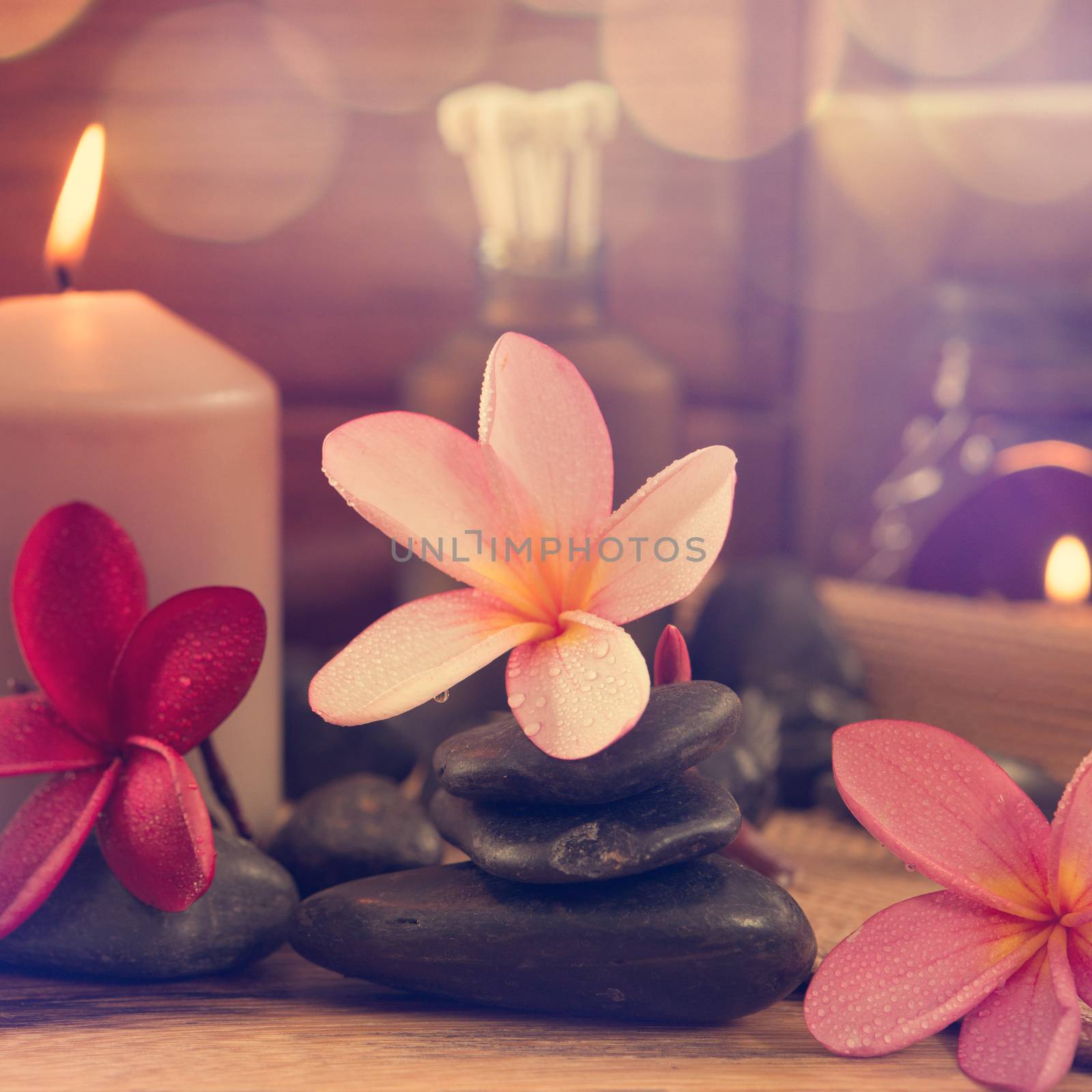 Spa setting with frangipani flower, essential oil, zen stones and aromatic candles on table, Zen concept in vintage retro style.
