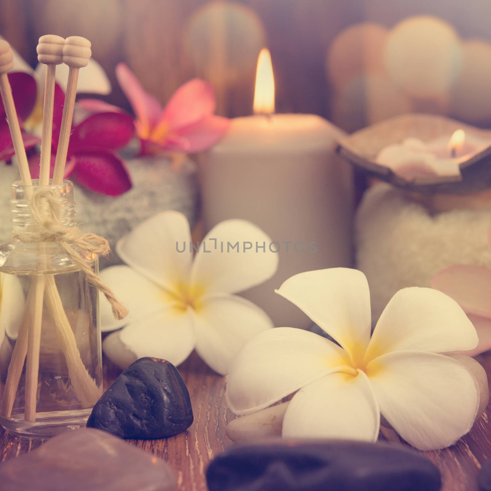 Wellness and spa concept with candles, frangipani flower, sandalwood and rattan sticks on massage table in vintage retro style.