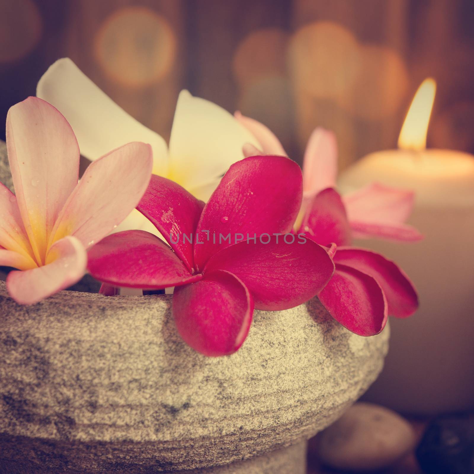 Spa still life setting with aromatic candles, frangipani flower, cold and hot stones in vintage retro style.