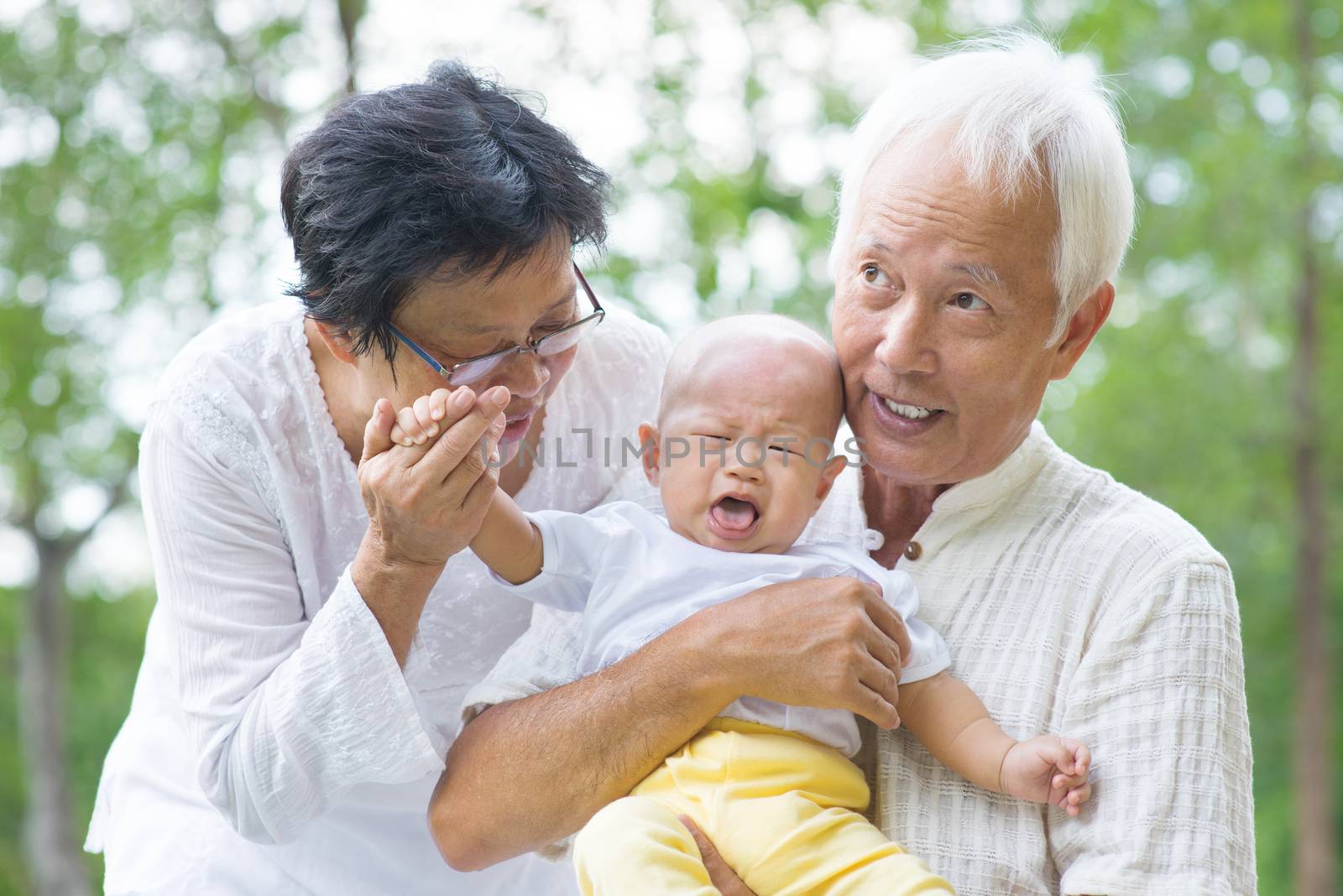 Asian crying baby comforted by grandparents at outdoor garden