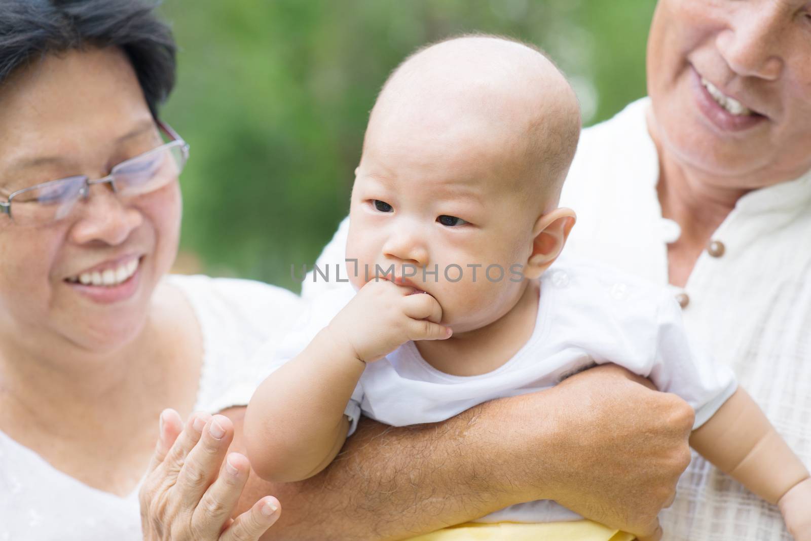 Asian grandparents playing with baby grandchild at outdoor garden.