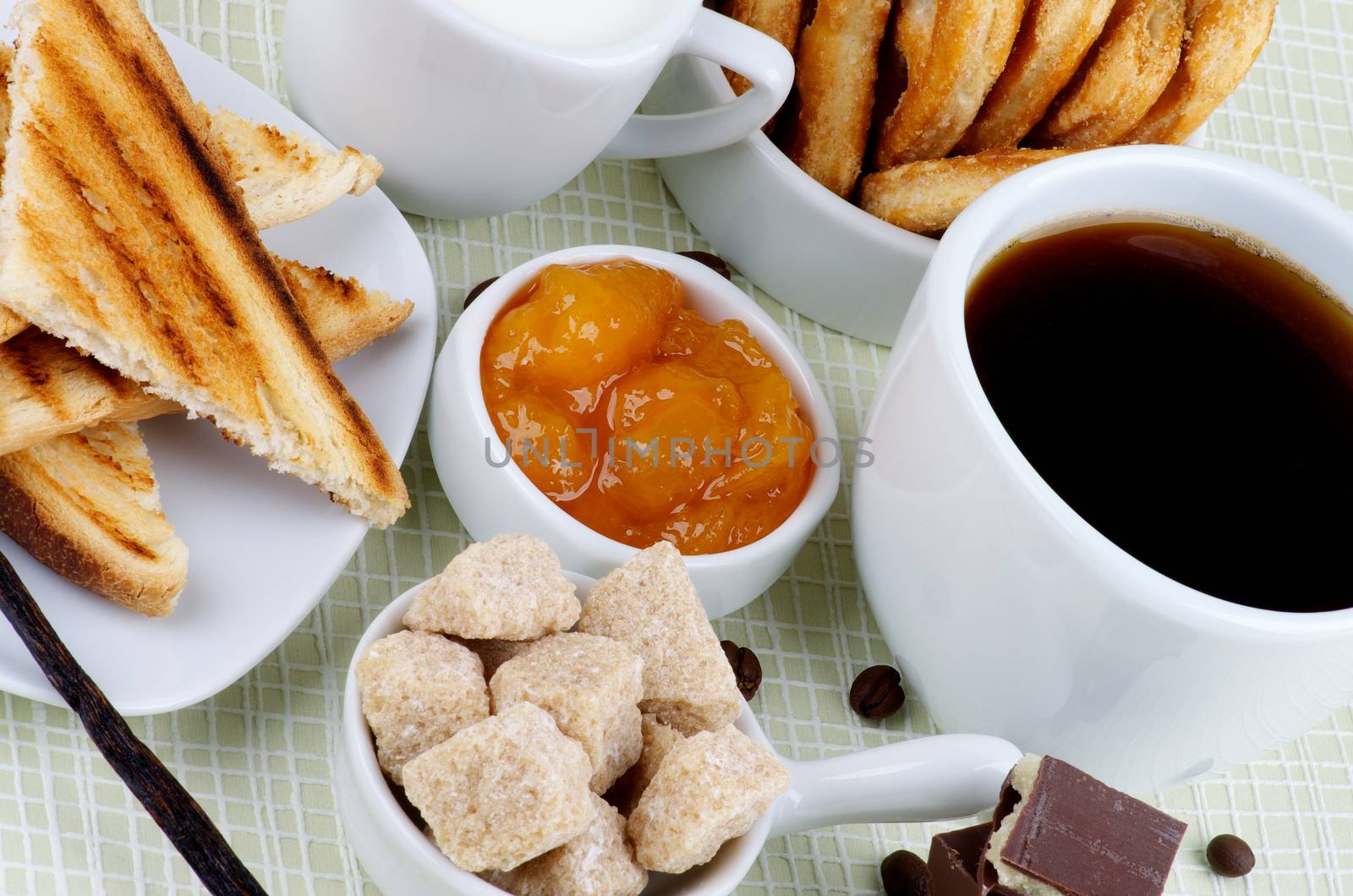Breakfast with Cup of Coffee, Chocolate, Sugar Cubes, Toasts, Apricot Jam, Milk and Puff Pastry on Checkered background