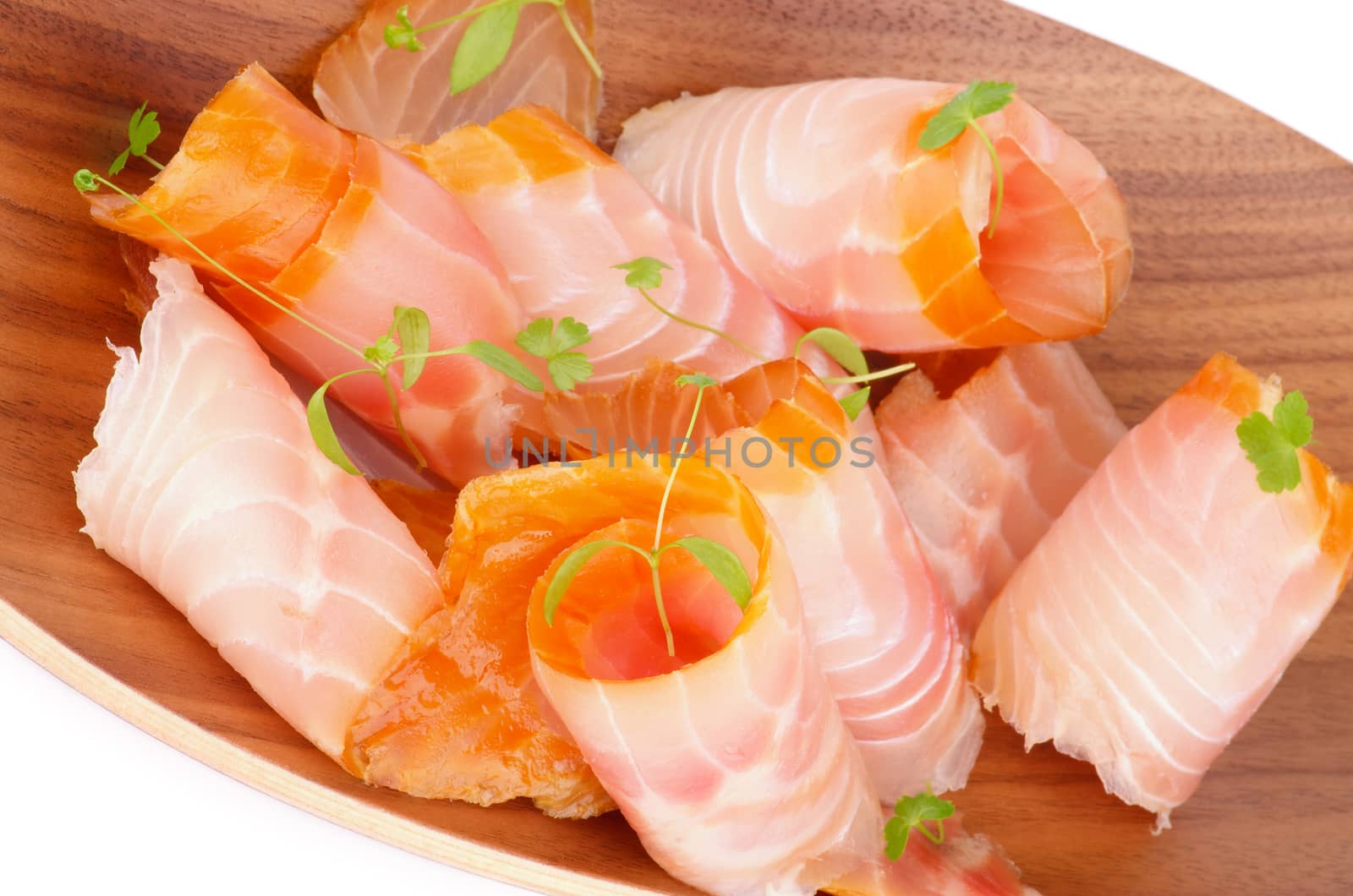 Snack of Swirled Slices of Delicious Smoked Sturgeon with Fresh Greens closeup on Wooden Plate