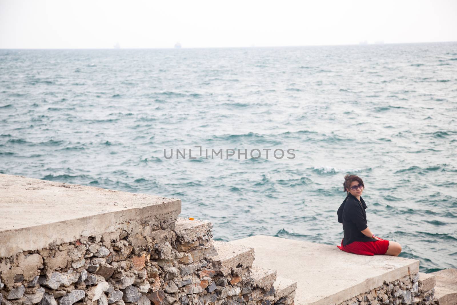 Asian women black shirt. Sitting on the sidewalk. A bridge near the ocean