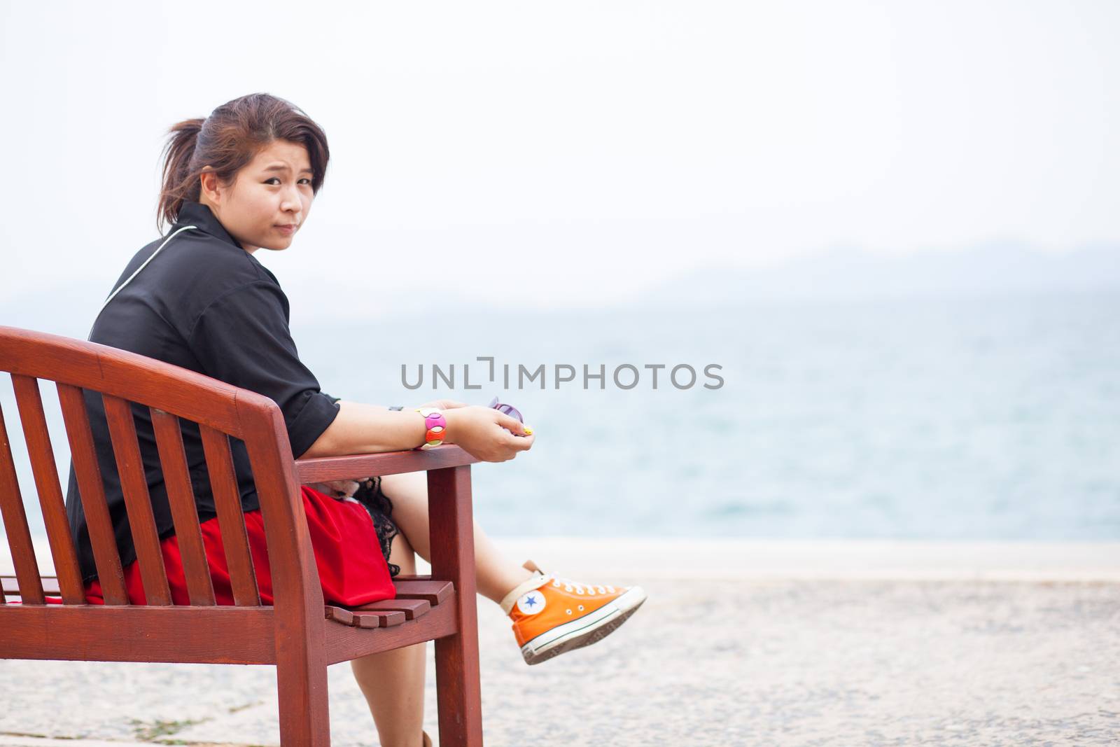 Asian women black shirt. Sitting on wooden bench. Adjacent to the corridor of the park.