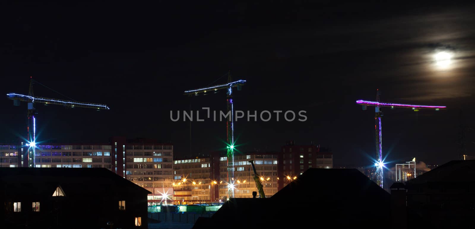 Construction cranes backlight against the sky with the moon