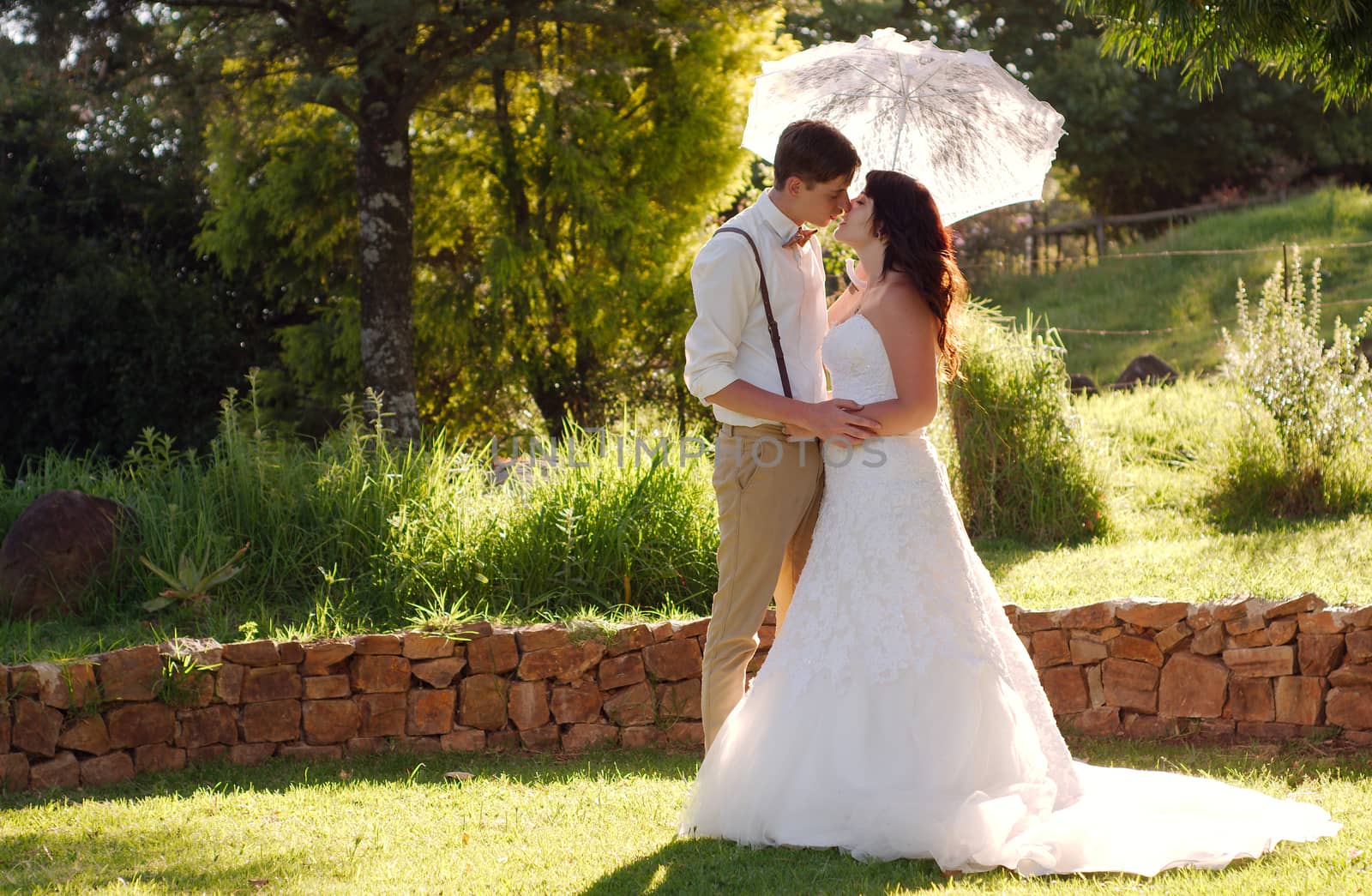 Bride and groom kissing with parasol in outside garden wedding ceremony