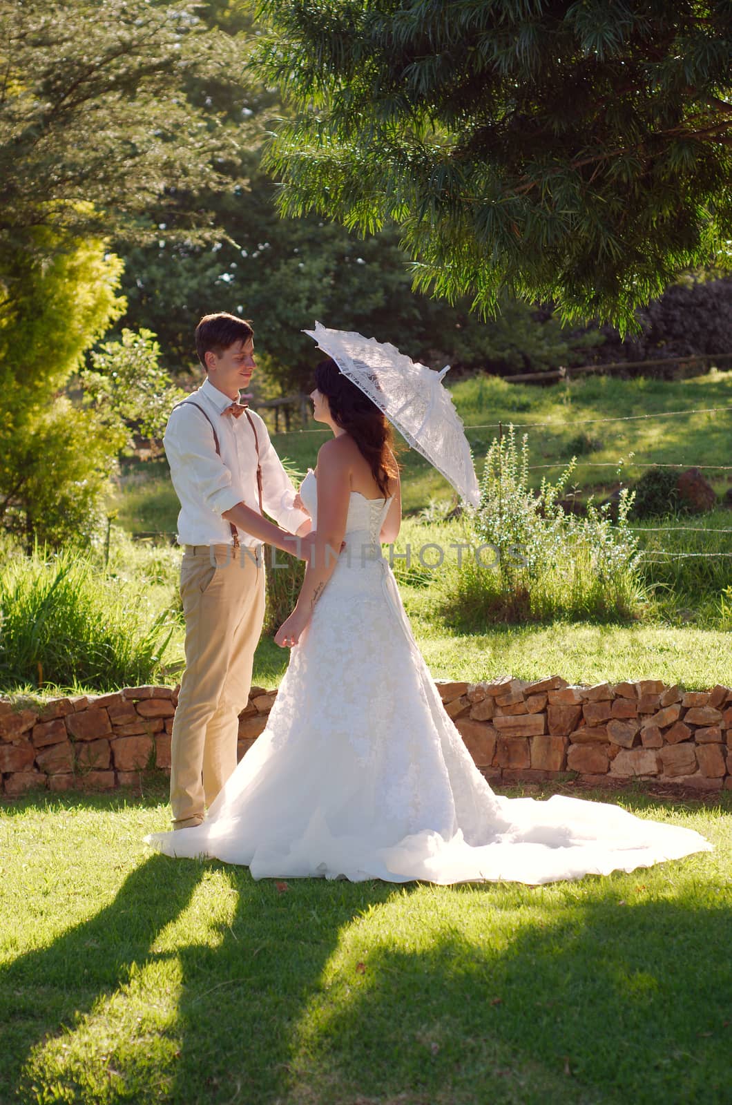 Bride and groom in garden wedding with parasol by alistaircotton