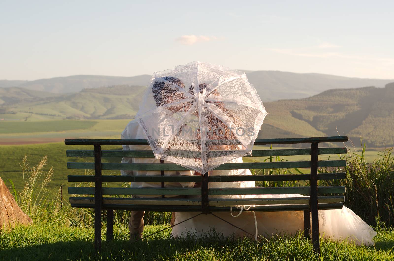 Bride and groom outside garden wedding on bench with African Natal Midlands mountain scenery background