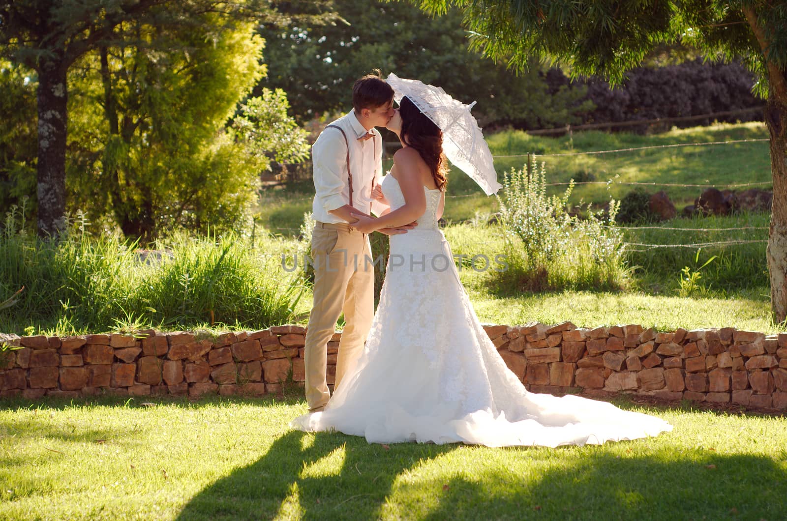 Bride and groom kissing with parasol in outside garden wedding ceremony