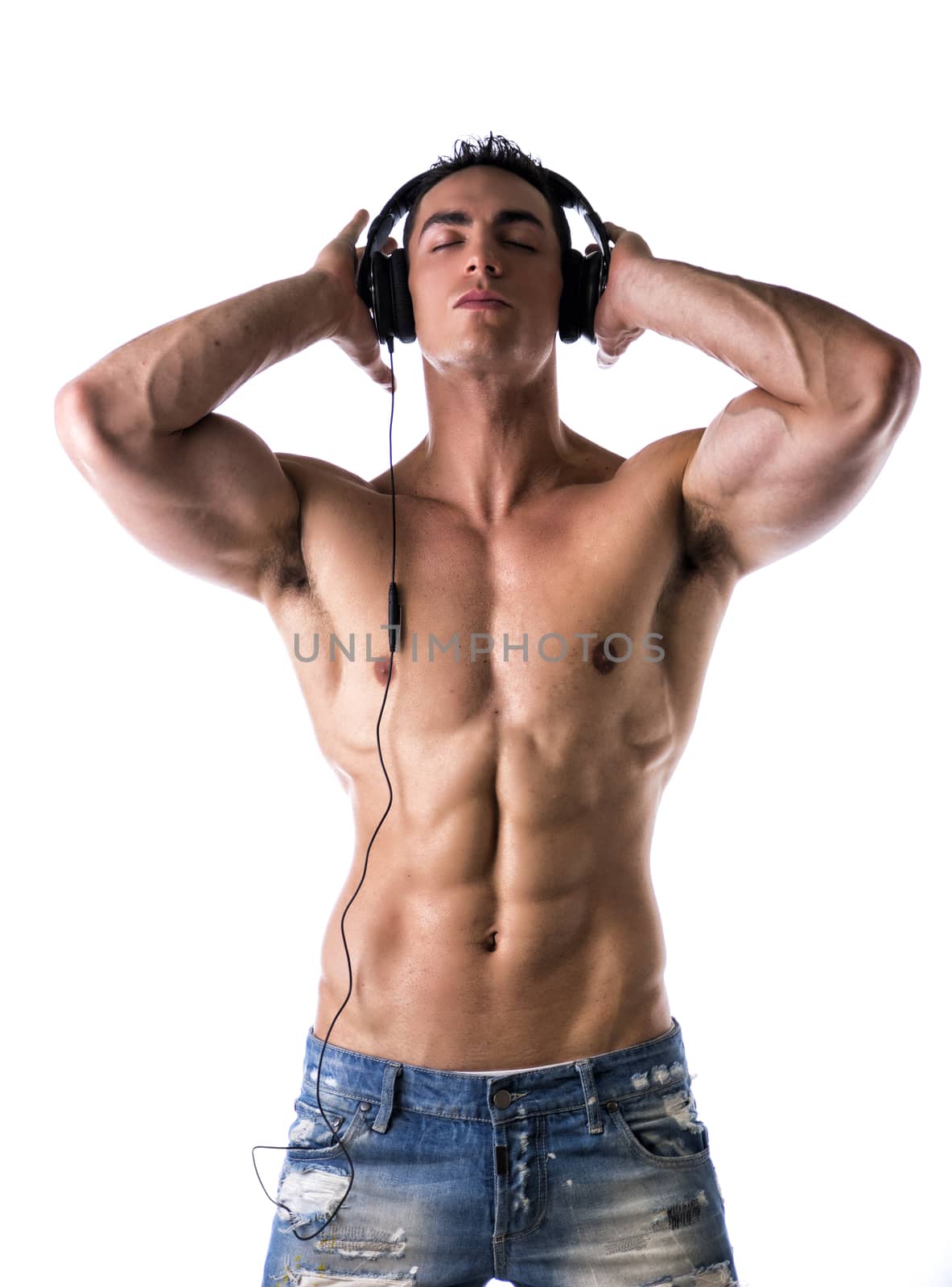 Muscular man shirtless, standing, listening to music on headphones, with eyes closed