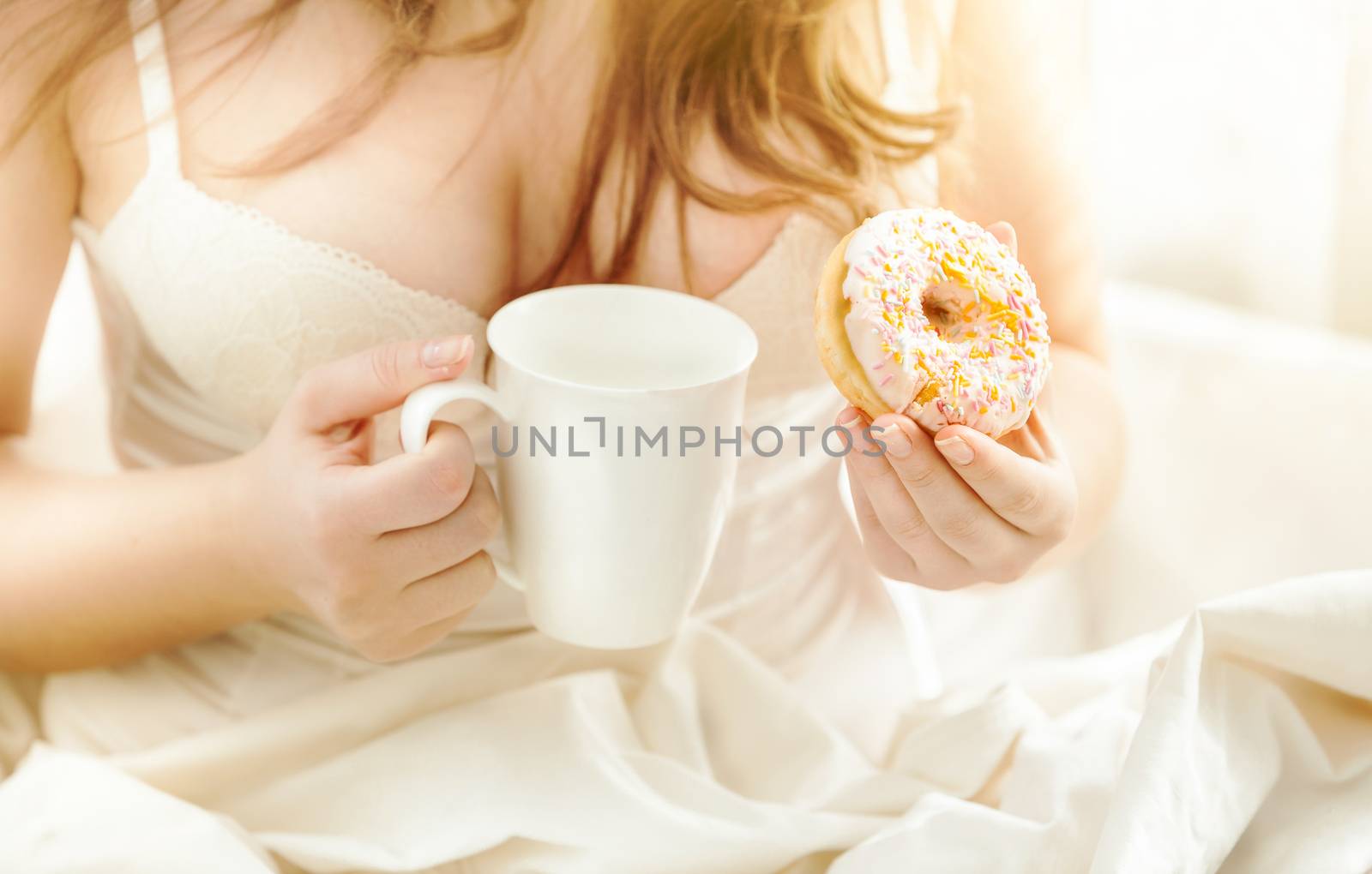 woman in bed holding donut and coffee at sunny morning by Kryzhov