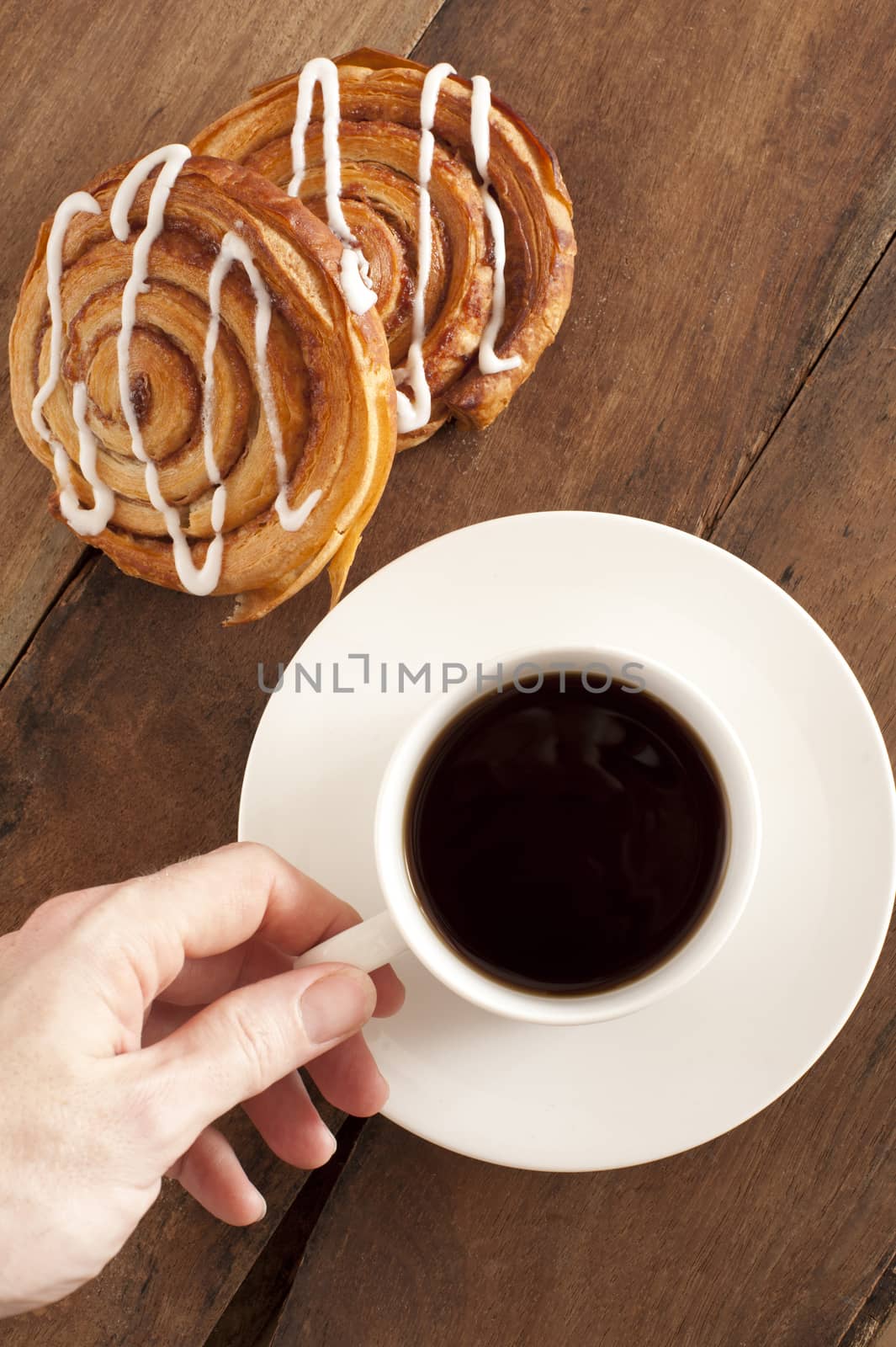 Overhead view of a mans hand reaching out to take a cup of rich espresso coffee and fresh Danish pastries for breakfast
