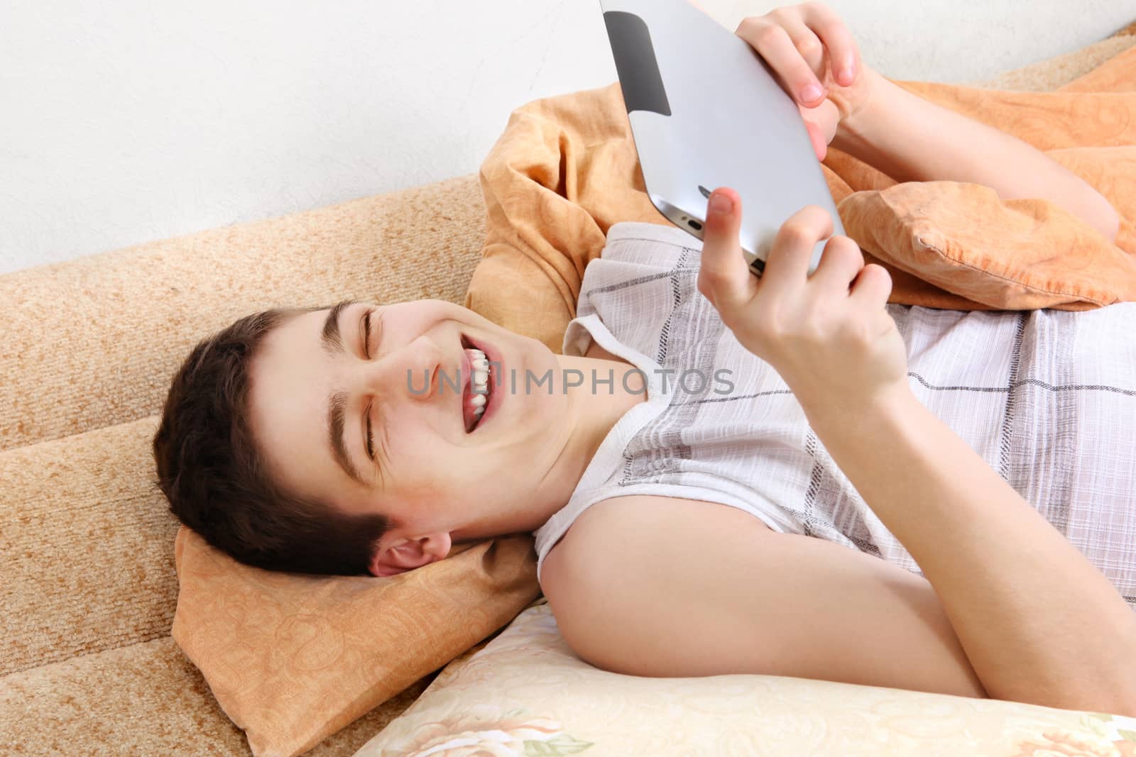 Cheerful Teenager using the Tablet Computer on the Sofa at the Home