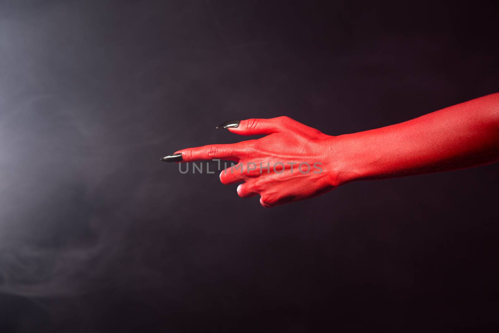 Red devil pointing hand with black sharp nails, extreme body-art, Halloween theme  