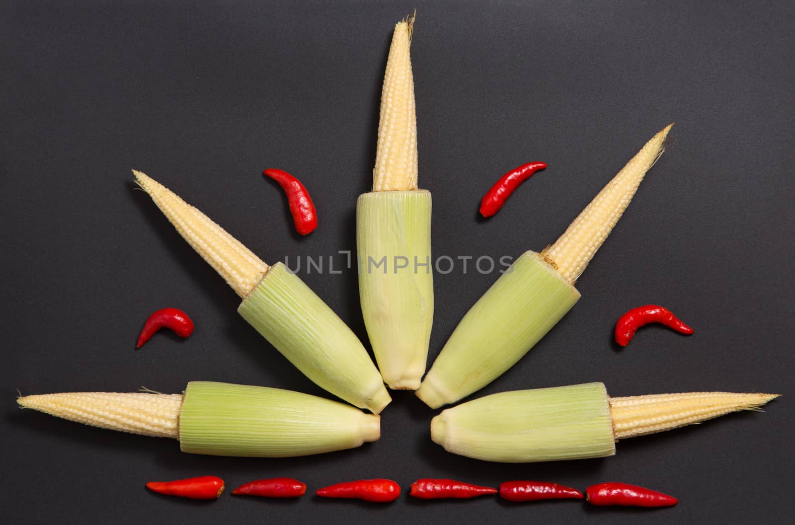 Fresh raw baby corn cobs with red non-stem chili peppers on gray background 