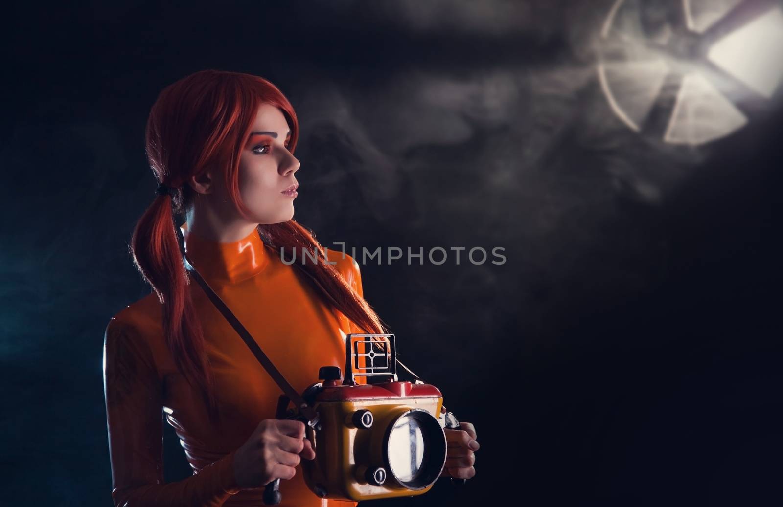 Portrait of sexy astronaut girl in orange latex catsuit holding vintage underwater camera case  