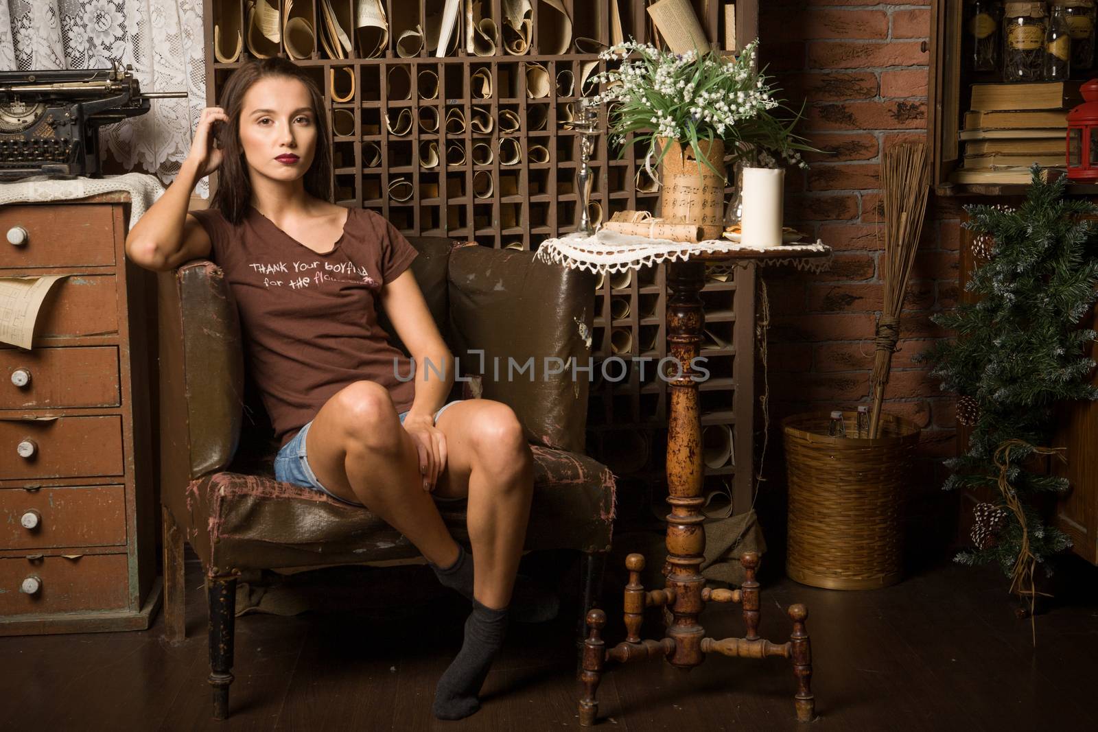 Young woman sits in an armchair on a background of vintage interior.