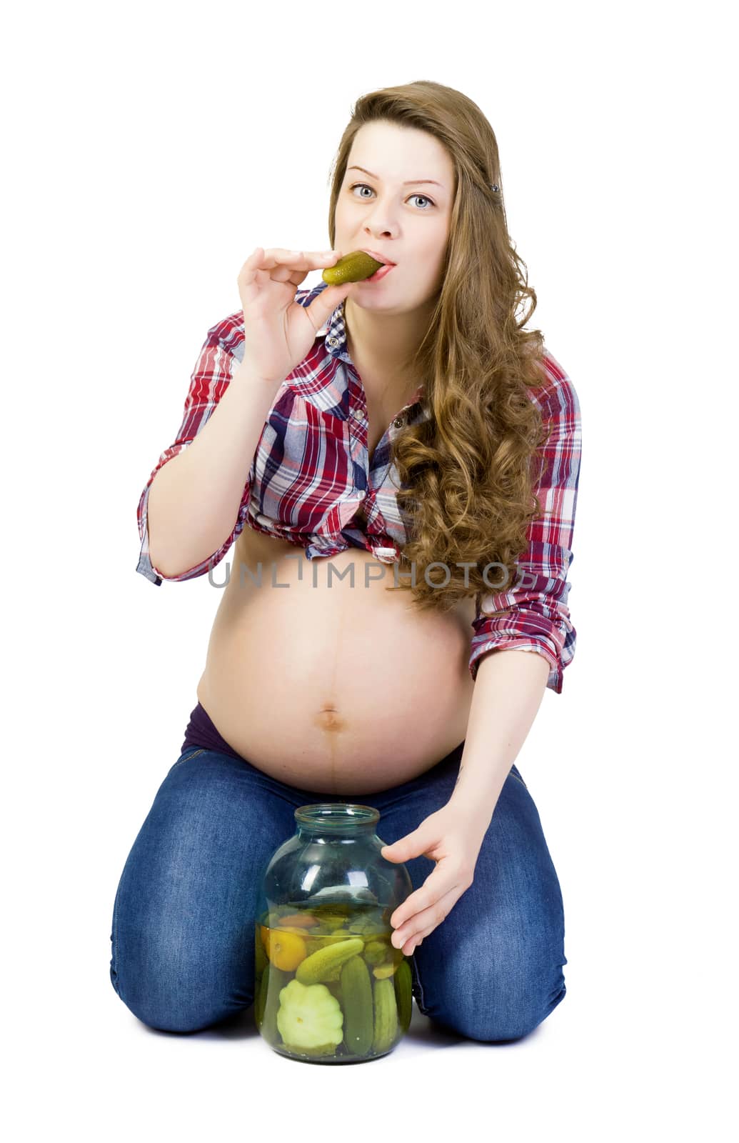 Pregnant young woman on a white background eats pickled cucumbers of a big glass jar