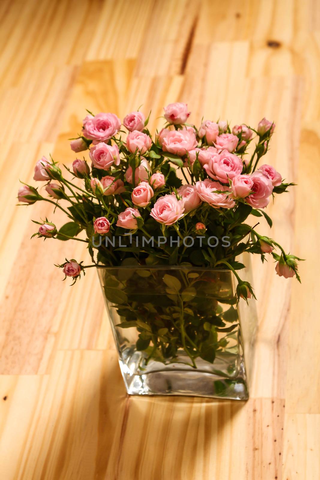Bunch of small pink Roses in a glass vase over a wooden table.
