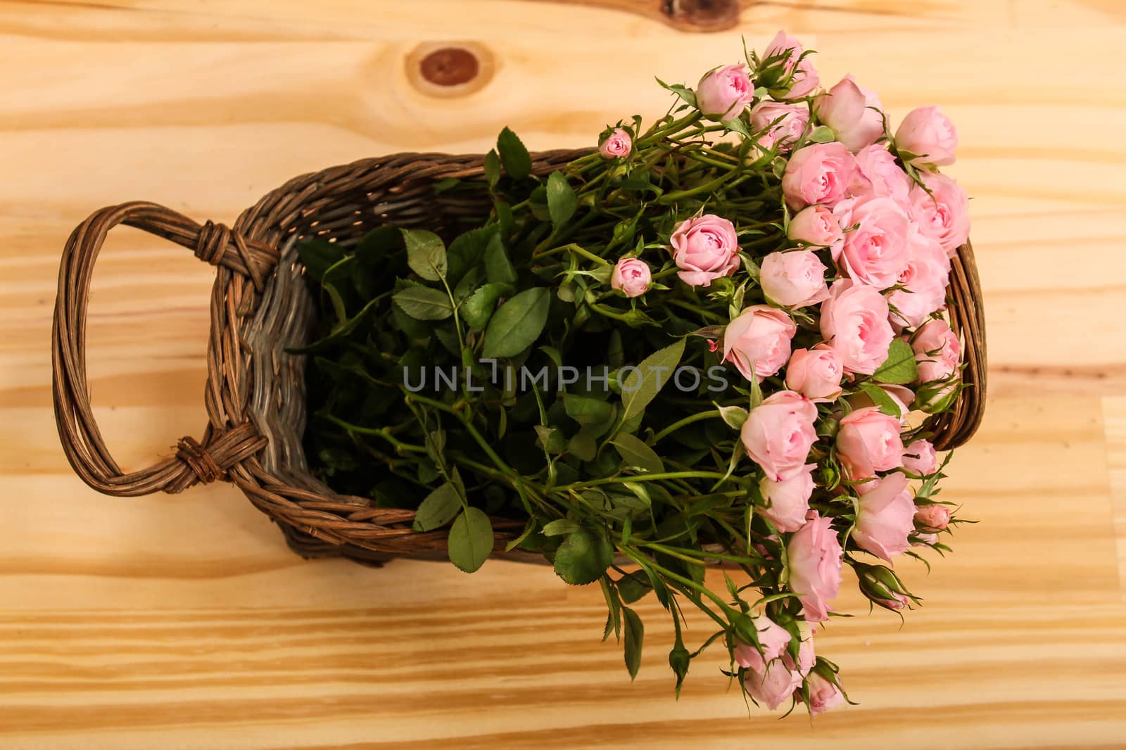 Bunch of small pink Roses in a basket over a wooden table.
