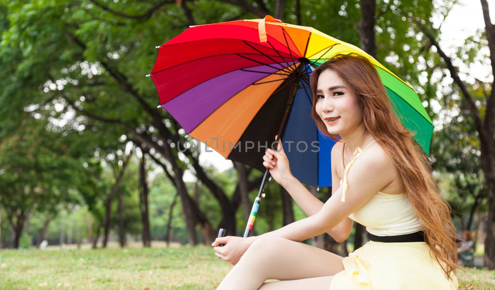 Woman with umbrella and sitting on the lawn. At the park