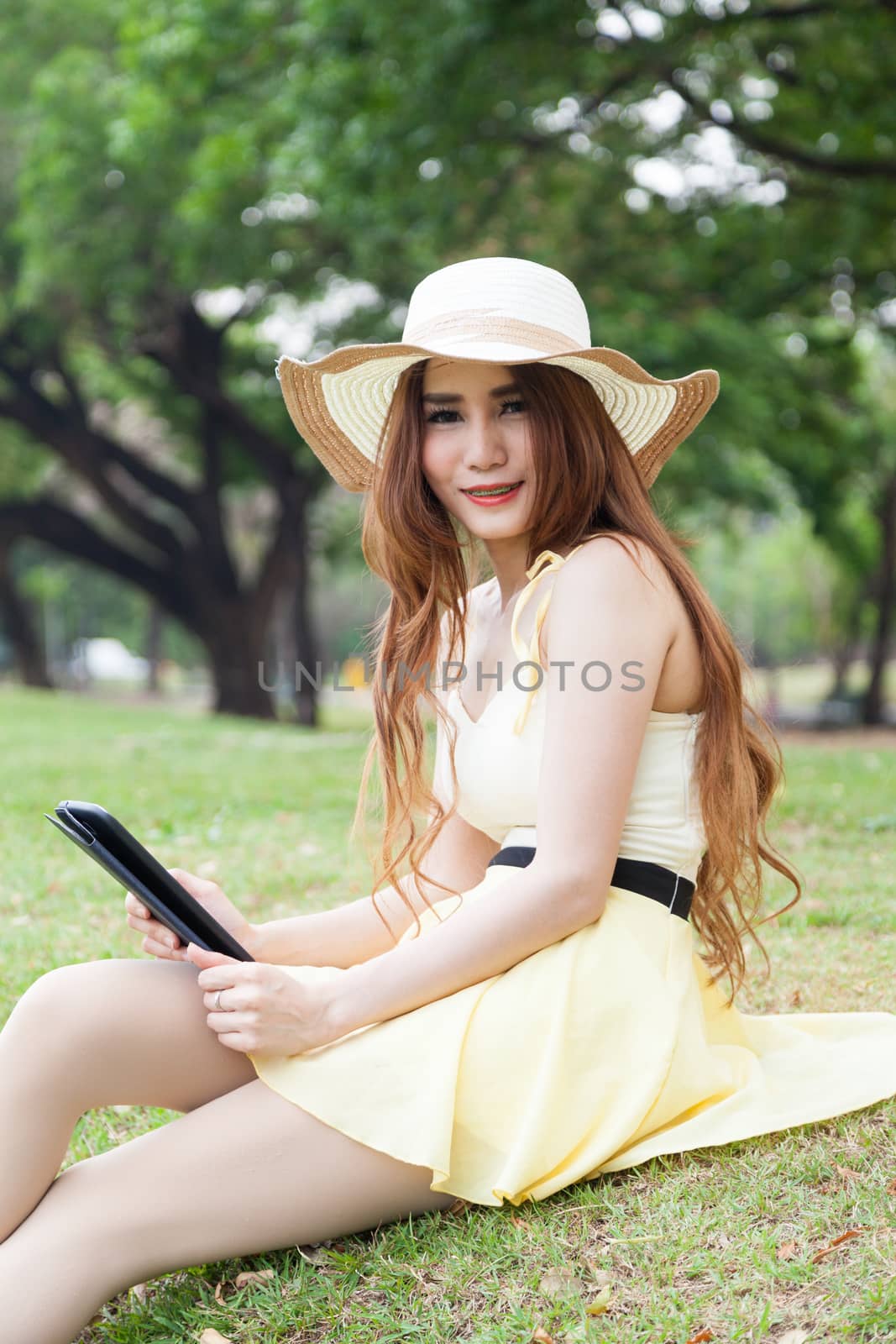Woman sitting on grass and using a tablet. Located within the park.