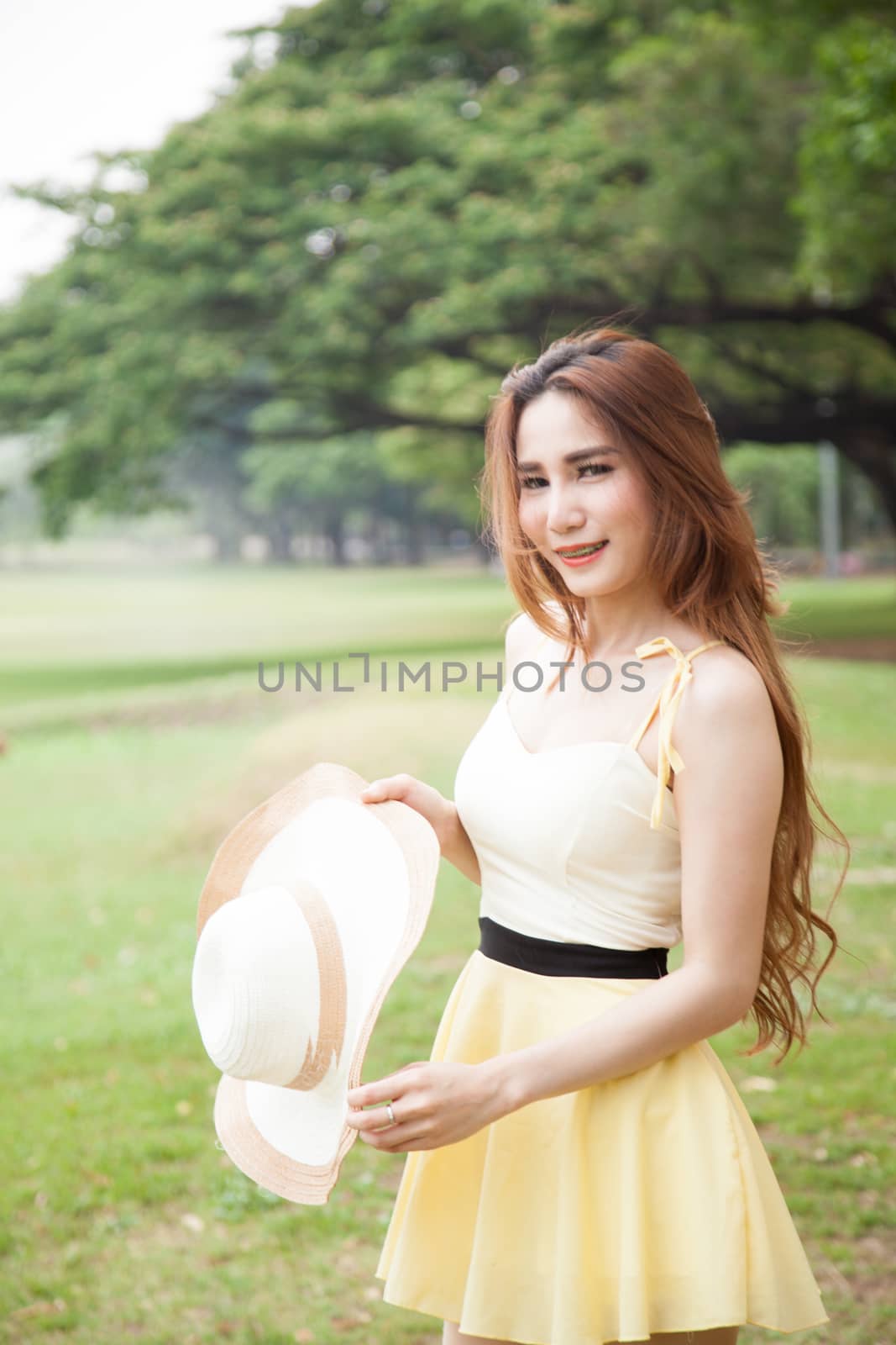 Woman holding a hat. Located at the lawn in the park.